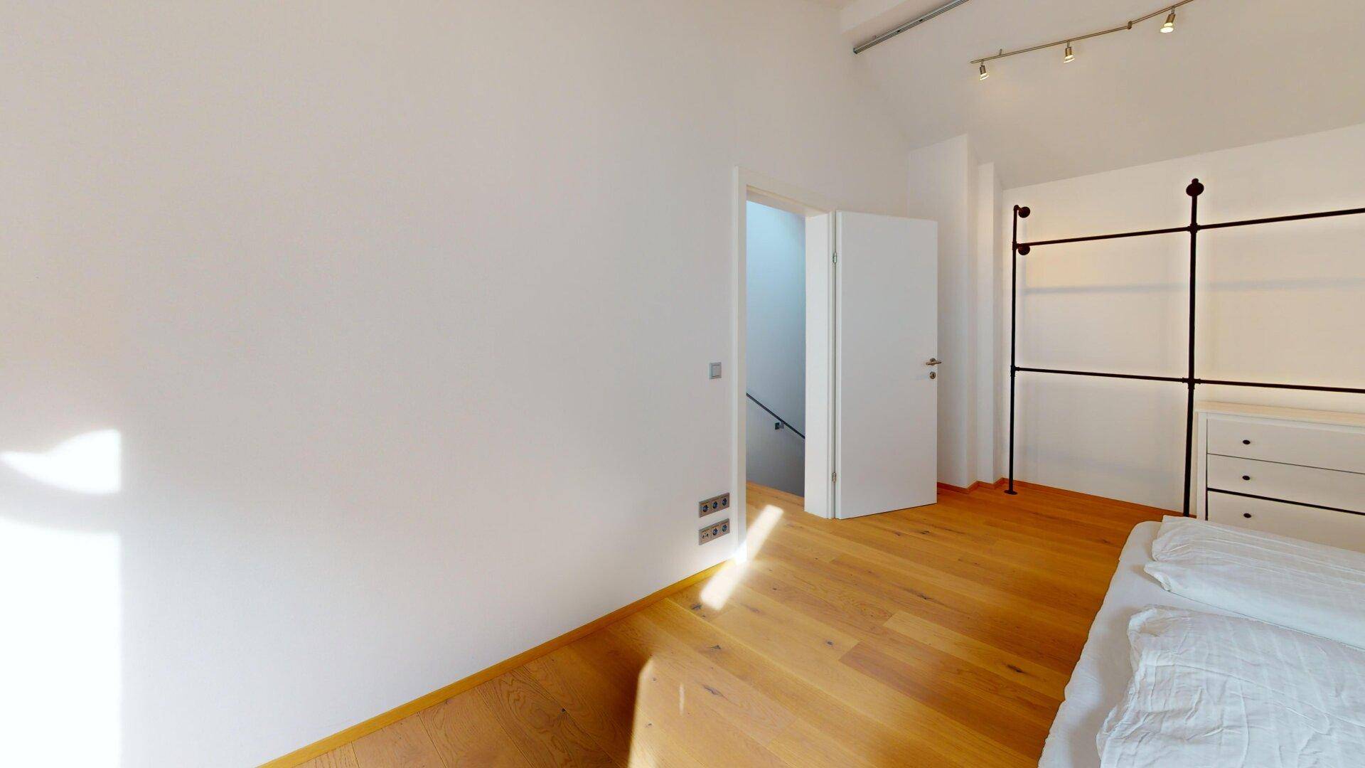 Schlafzimmer mit Holzboden, Zugang zum Treppenhaus und offenem Kleiderschranksystem.