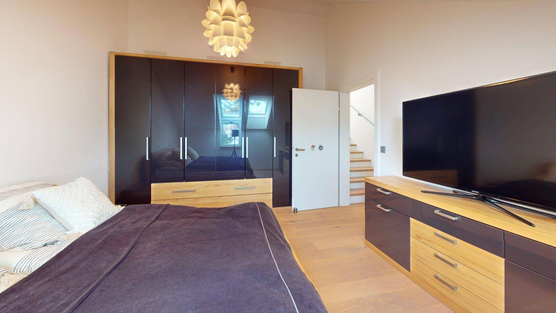 Schlafzimmer mit großem dunklem Kleiderschrank, Holzboden und Fernseher auf einem Sideboard.