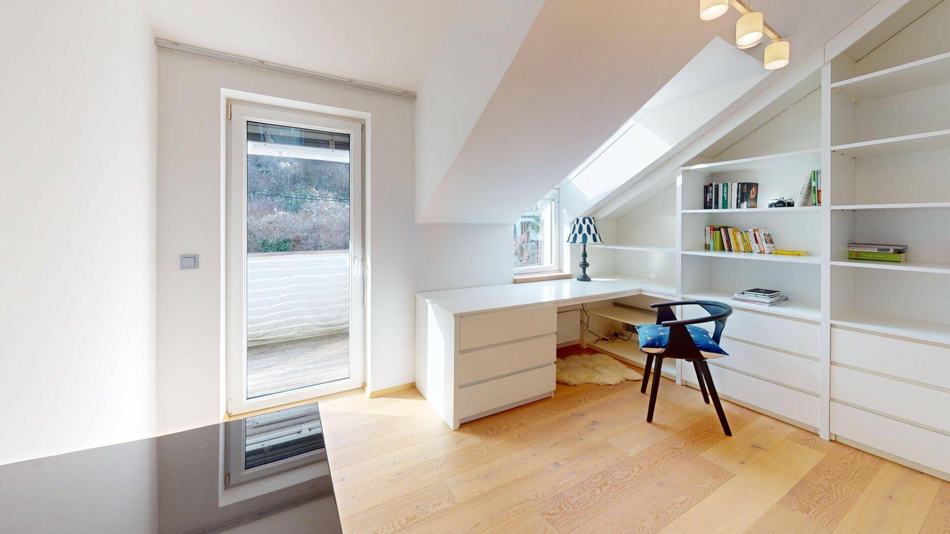 Helles Arbeitszimmer mit Schreibtisch, Bücherregalen und Zugang zu einem Balkon.