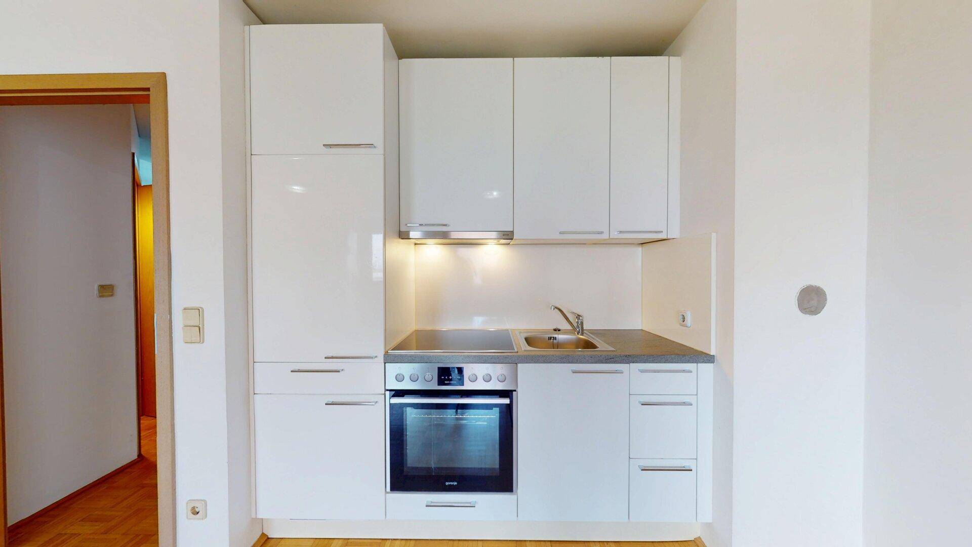 Moderne Küchenzeile mit weißen Hochglanzfronten, integriertem Backofen und Dunstabzugshaube.