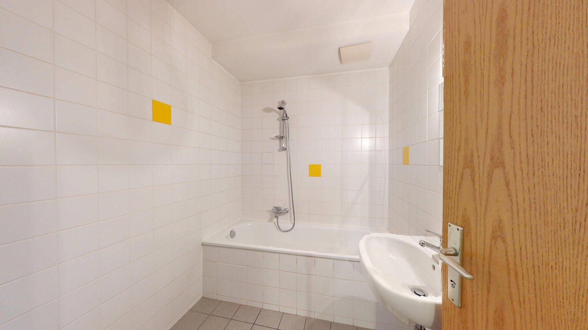Helles Badezimmer mit weiß gefliesten Wänden, Badewanne mit Duschfunktion und Waschbecken.