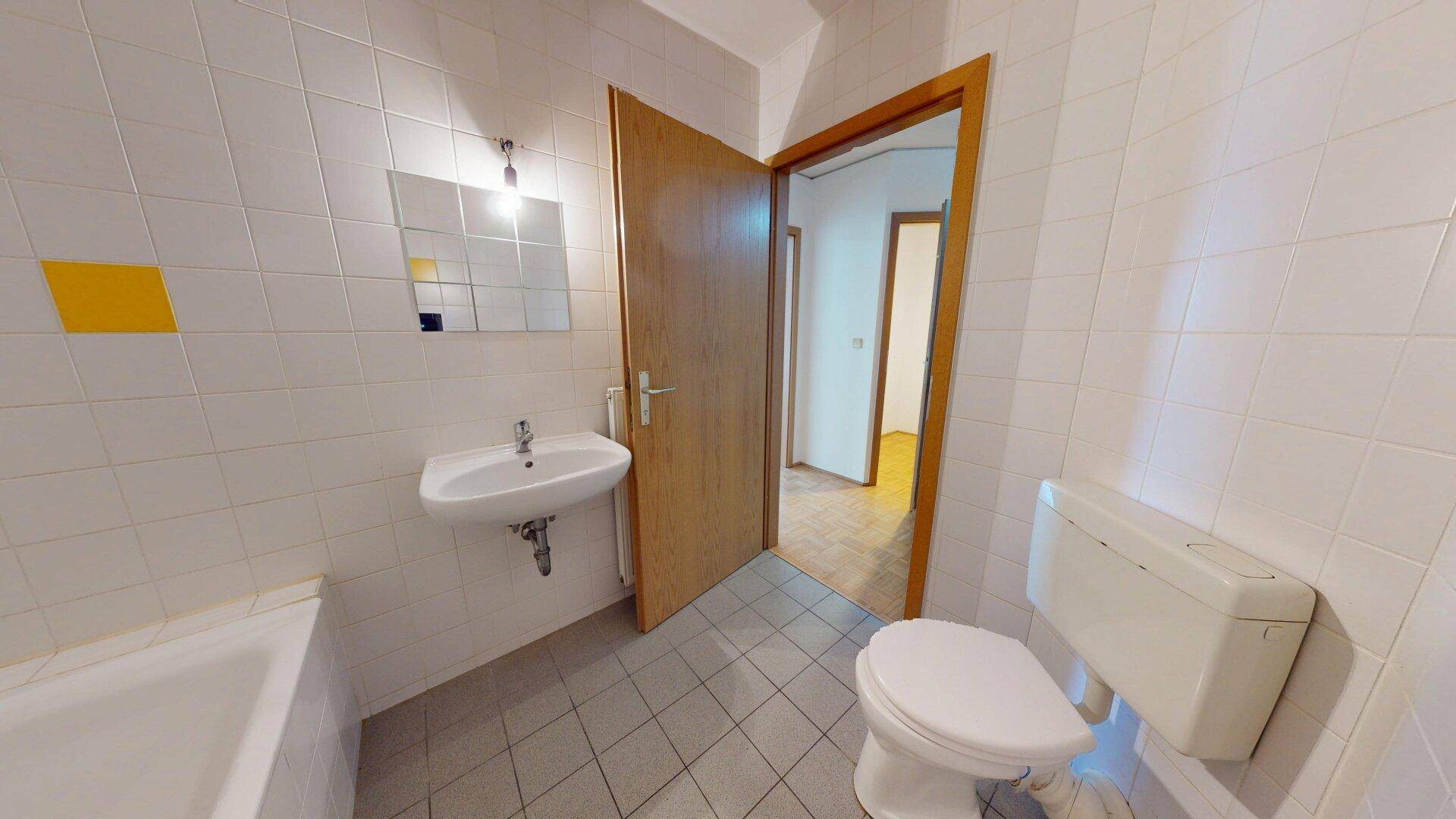 Badezimmer mit WC, Waschbecken, Spiegel und weiß-gelben Fliesen an den Wänden.