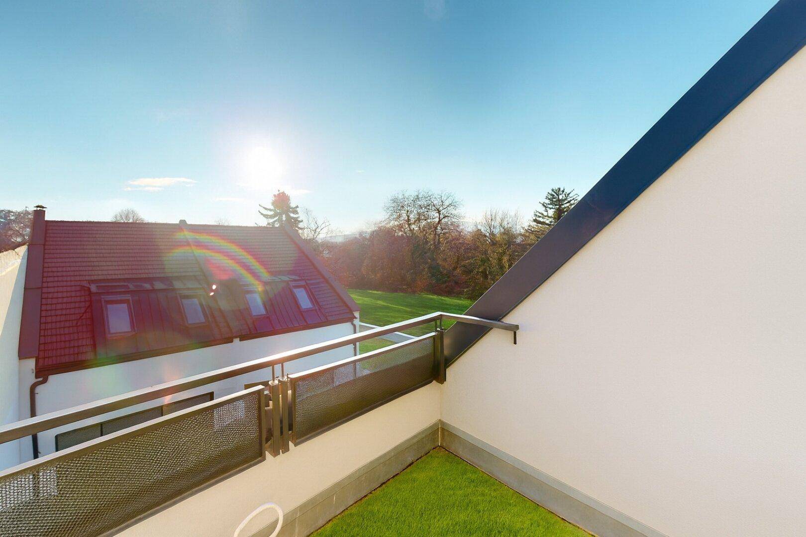 Kleiner Balkon mit Kunstrasen und Blick auf die umliegenden Dächer und Bäume.