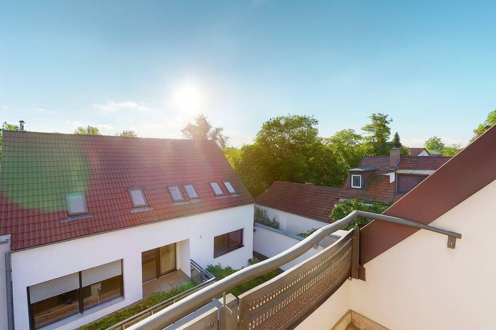 Balkon mit Metallgeländer und weitem Blick über Dächer und grüne Landschaft.