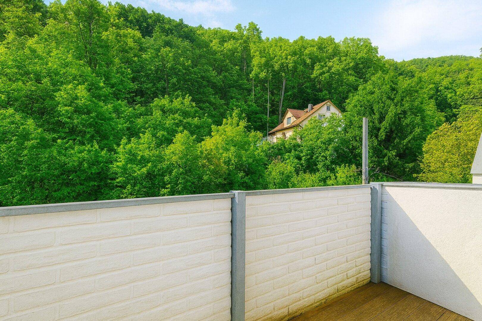 Balkon mit weißer Ziegelmauer und Blick auf grüne Hügel sowie ein verstecktes Haus.