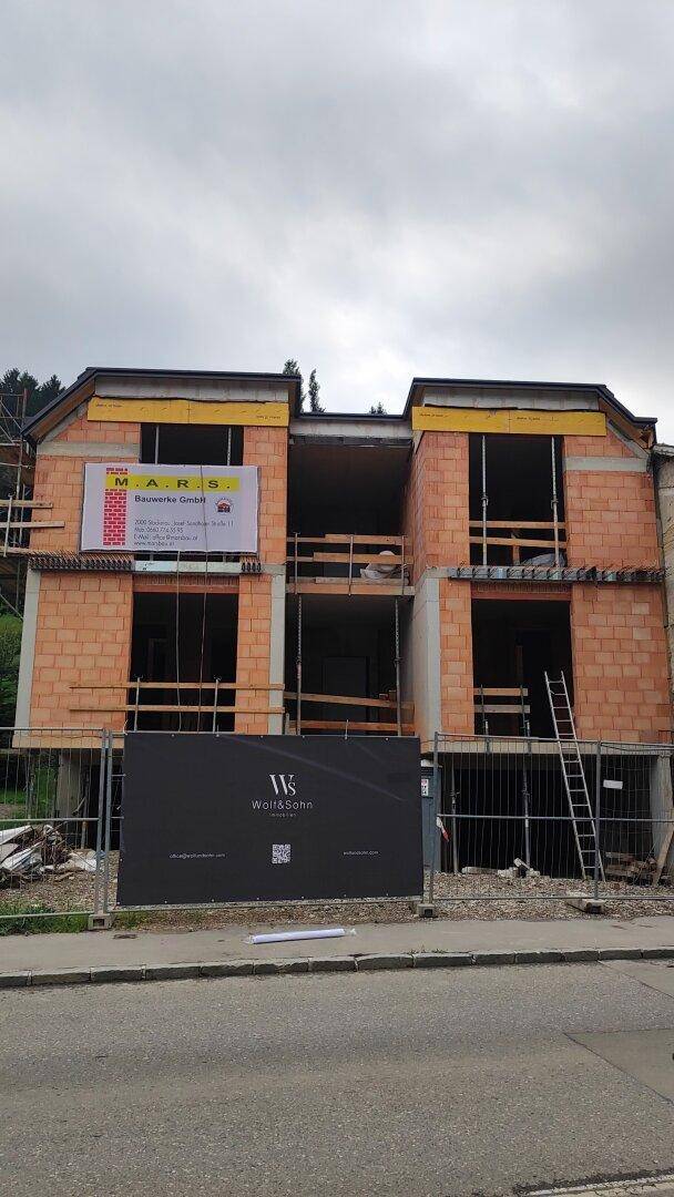 Baustelle eines Mehrfamilienhauses mit sichtbaren Ziegelwänden und Baugerüst.