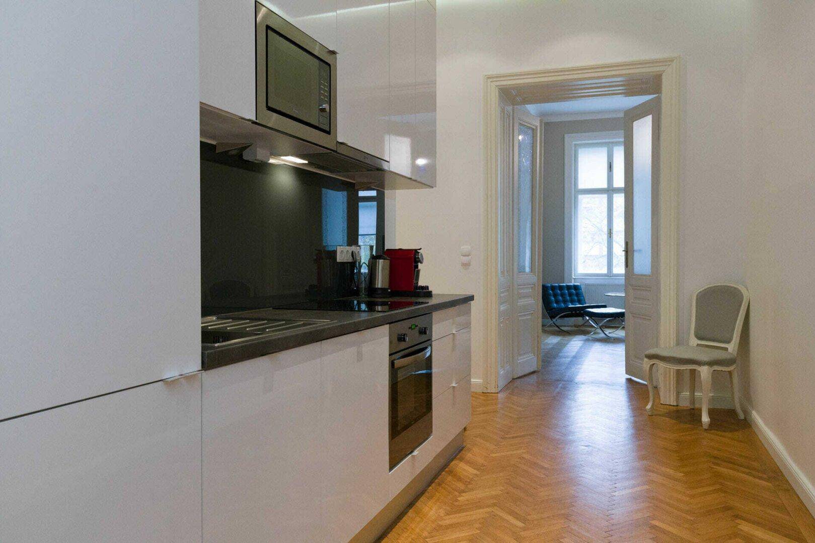 Moderne Küchenzeile mit weißen Hochglanzschränken, integrierten Geräten und Fischgrätparkett.