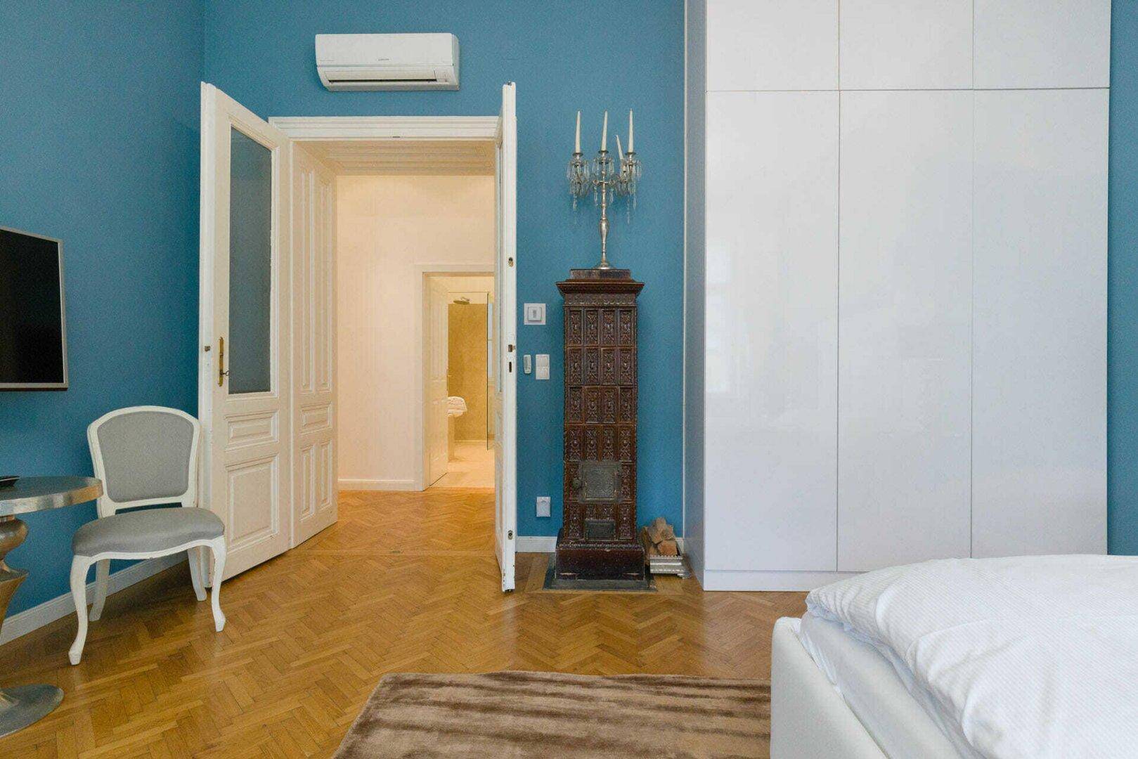 Schlafzimmer mit blauer Wand, weißem Einbauschrank und einem traditionellen Kachelofen.