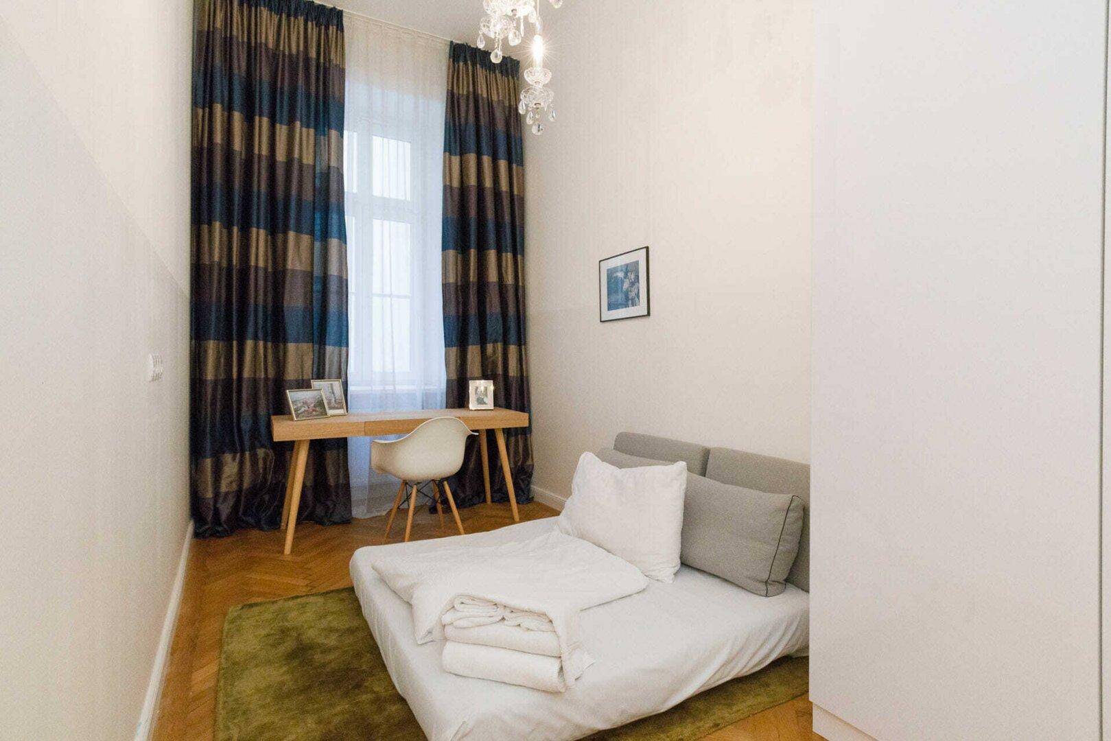 Kleines Schlafzimmer oder Arbeitszimmer mit Schreibtisch, Bett und gestreiften Vorhängen.