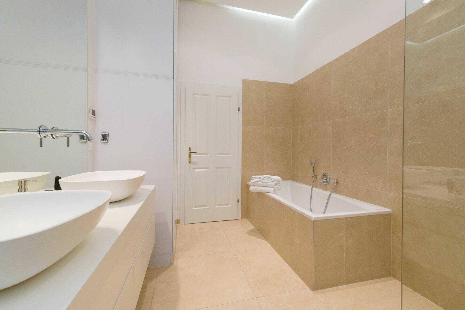 Modernes Badezimmer mit doppelten Aufsatzwaschbecken, Badewanne und beigefarbenen Fliesen.