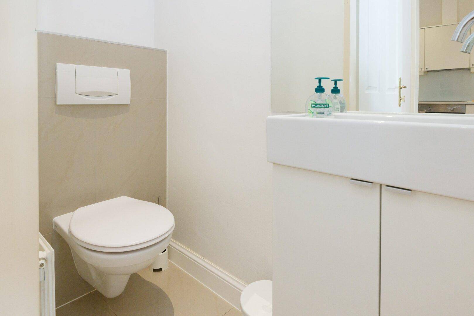 Separates Gäste-WC mit wandhängender Toilette, Einzelwaschbecken und hellen Fliesen.