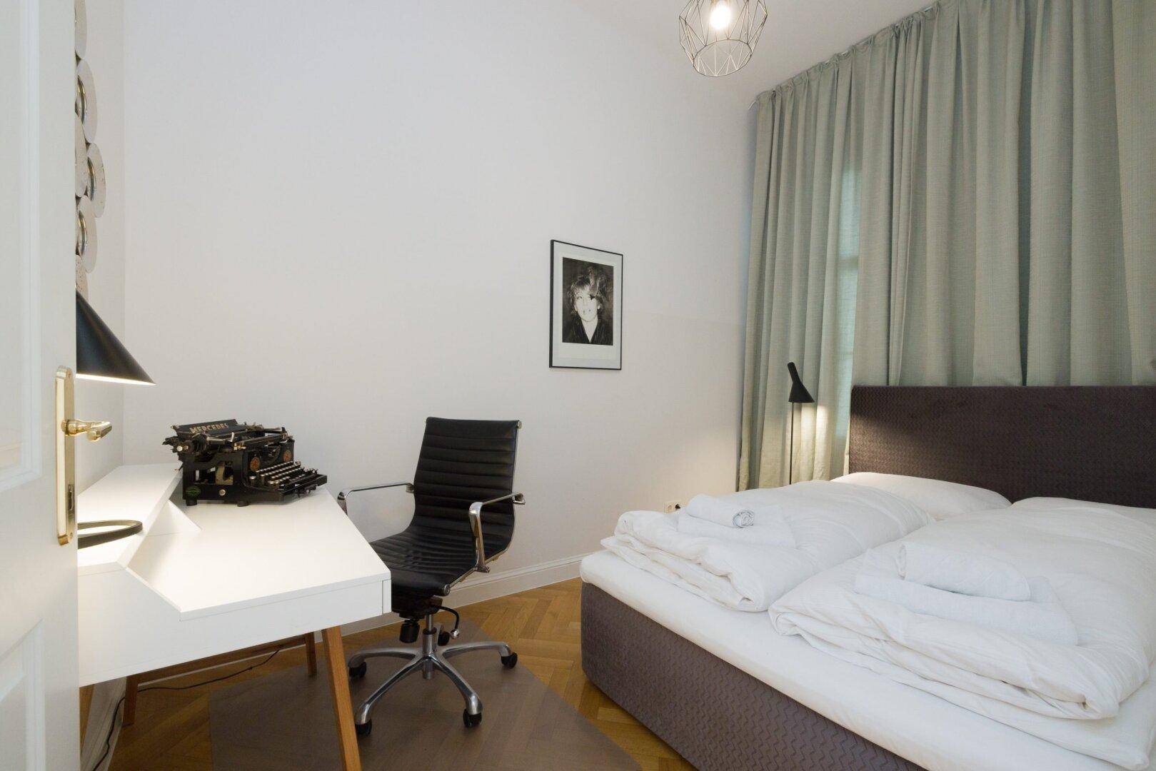Ruhiger Arbeitsbereich mit Schreibtisch, Bürostuhl und einem Bett, ideal für Gäste oder Home-Office.
