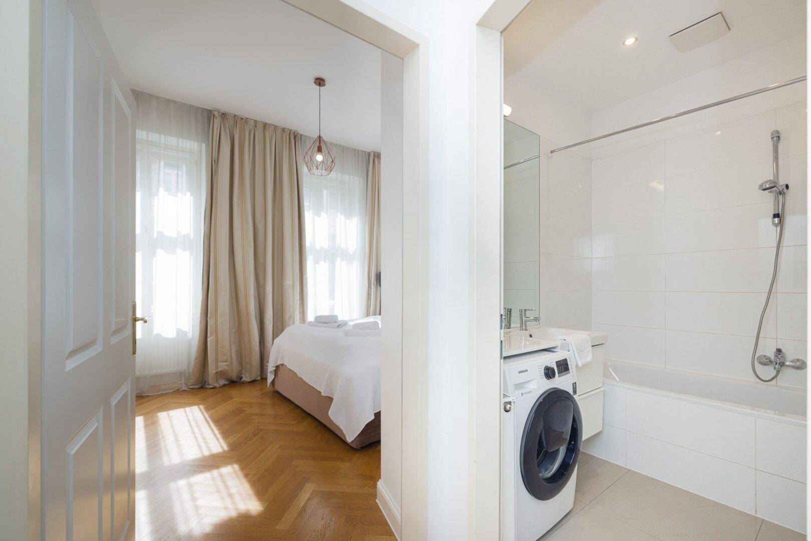 Blick vom Schlafzimmer in das angrenzende Badezimmer mit Badewanne und Waschmaschine.