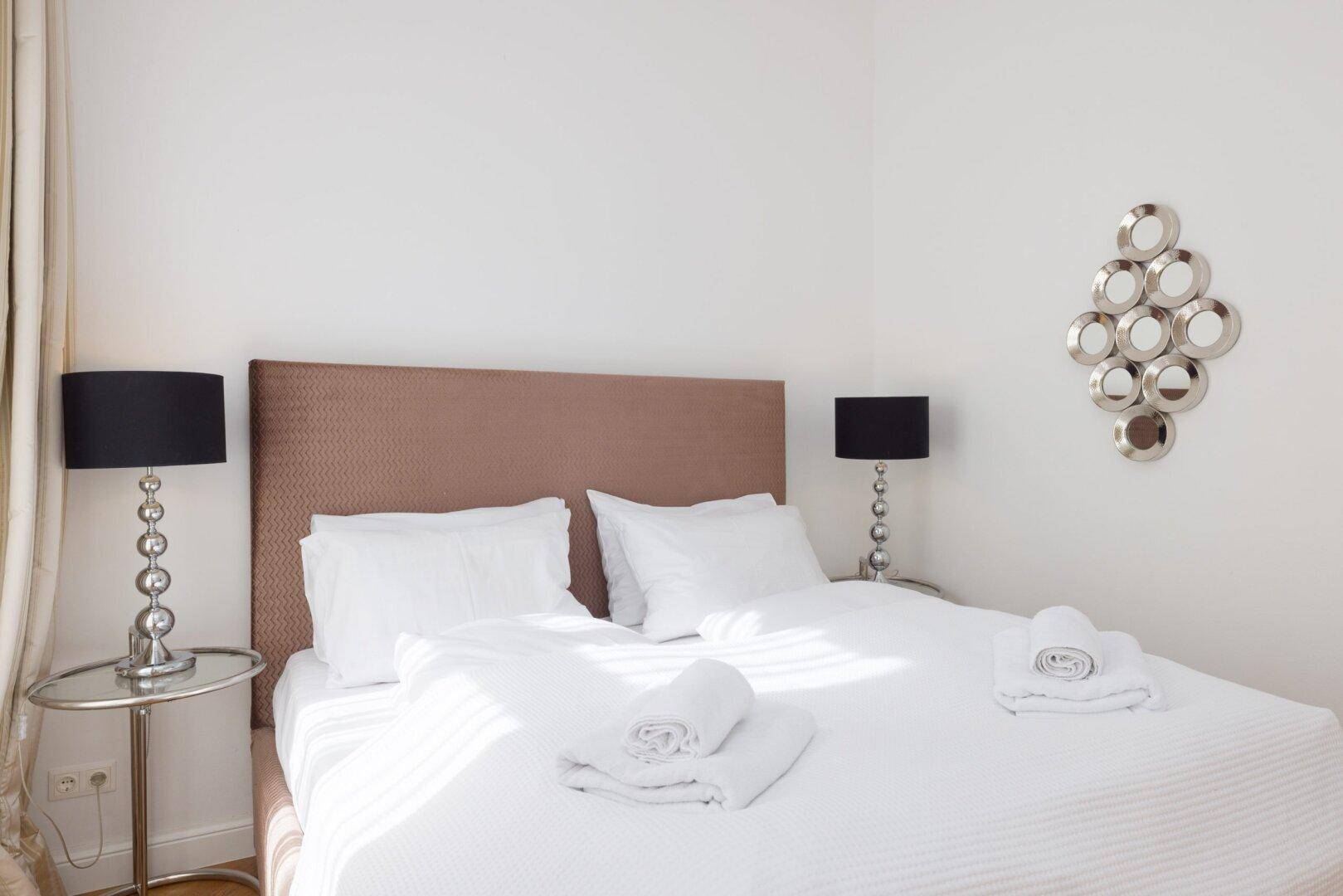 Gut beleuchtetes Schlafzimmer mit Doppelbett, Parkettboden und eleganten Nachttischlampen.