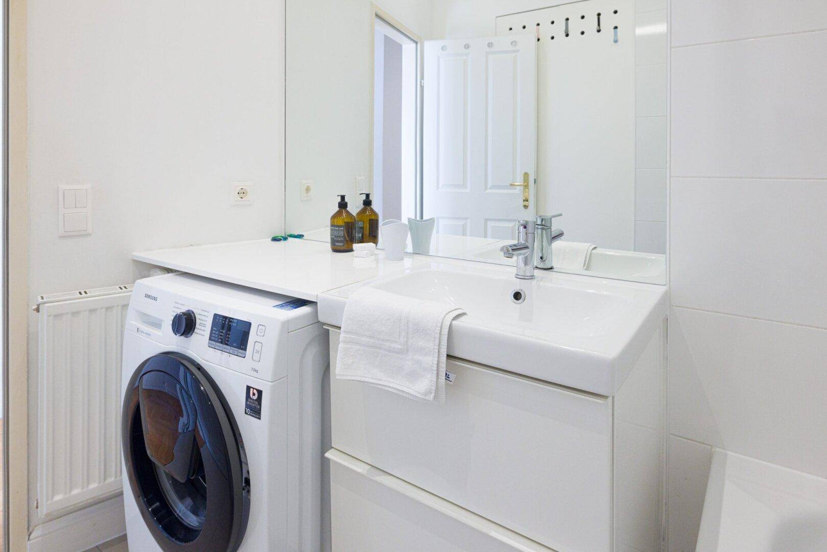 Modernes Badezimmer mit Einzelwaschbecken, Waschmaschine und großem Spiegel über dem Waschtisch.