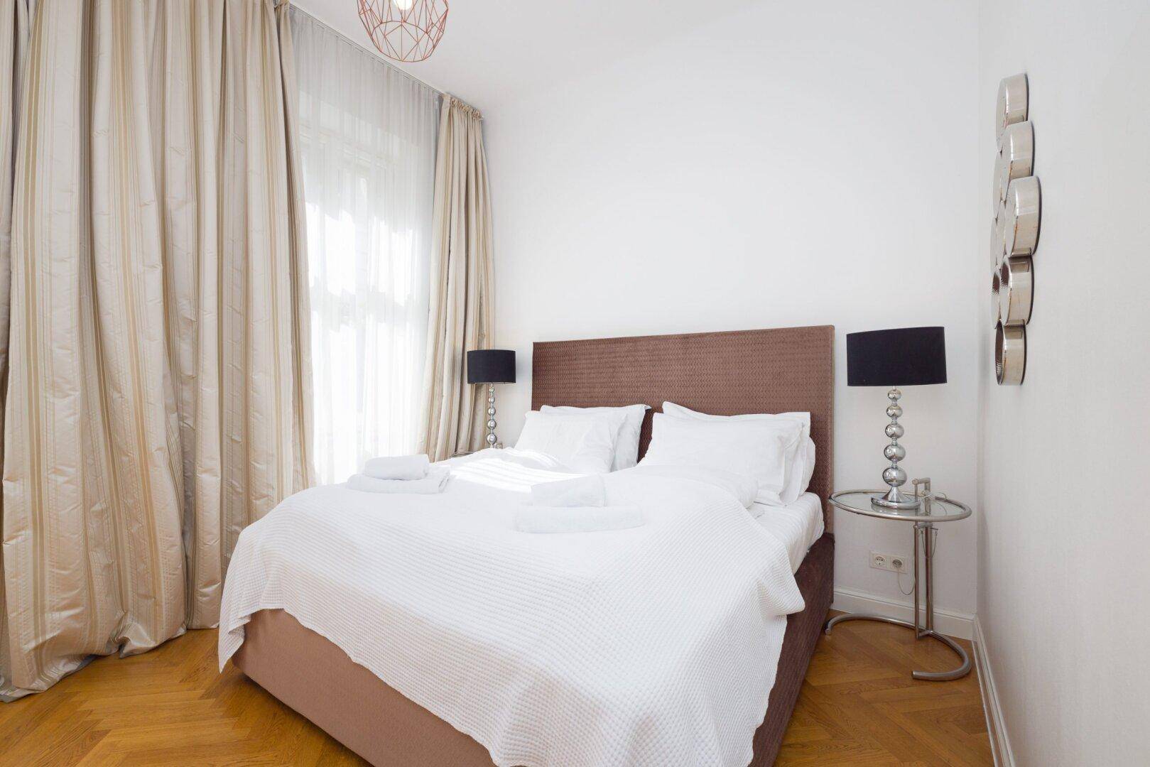 Gemütliches Schlafzimmer mit Doppelbett, Parkettboden und hellen Vorhängen am Fenster.