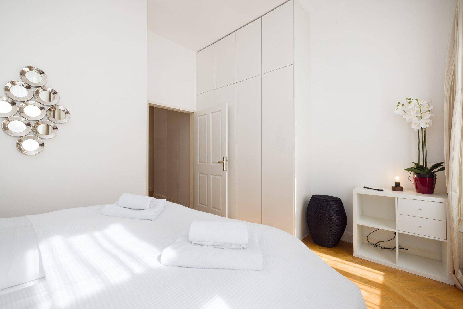 Helles Schlafzimmer mit großem Einbauschrank, Parkettboden und dekorativer Orchidee.