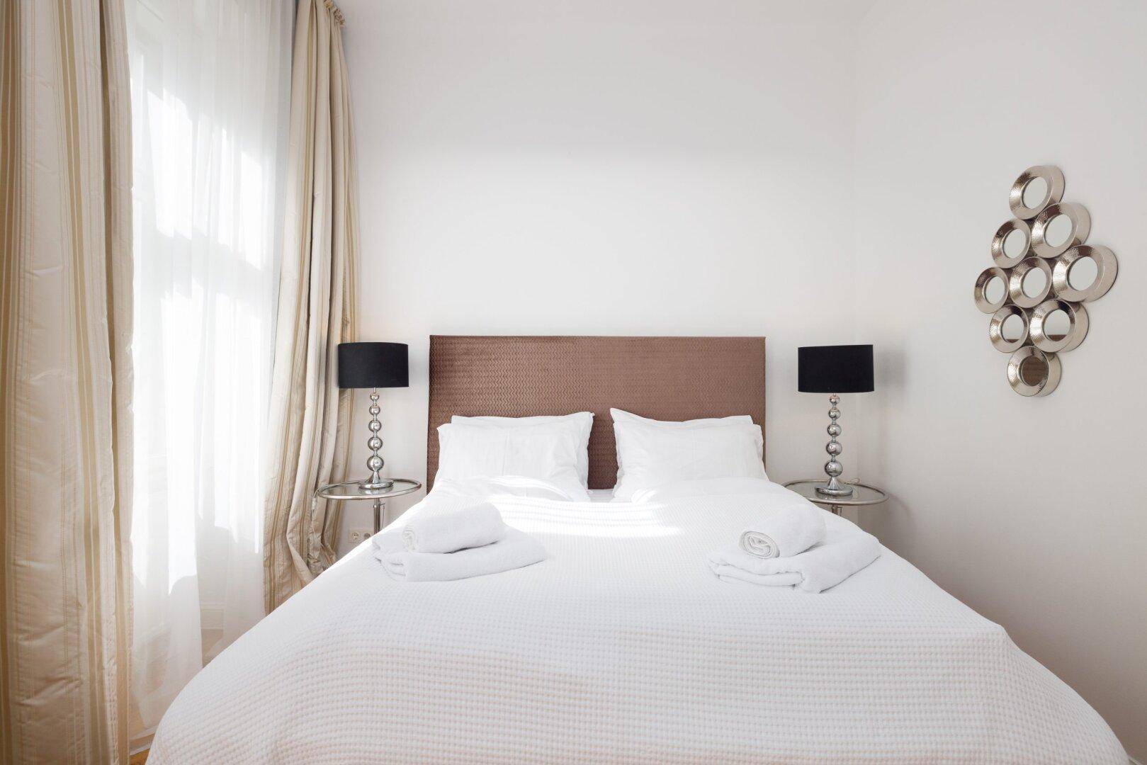 Helles Schlafzimmer mit komfortablem Doppelbett, Nachttischen und dekorativem Wandspiegel.
