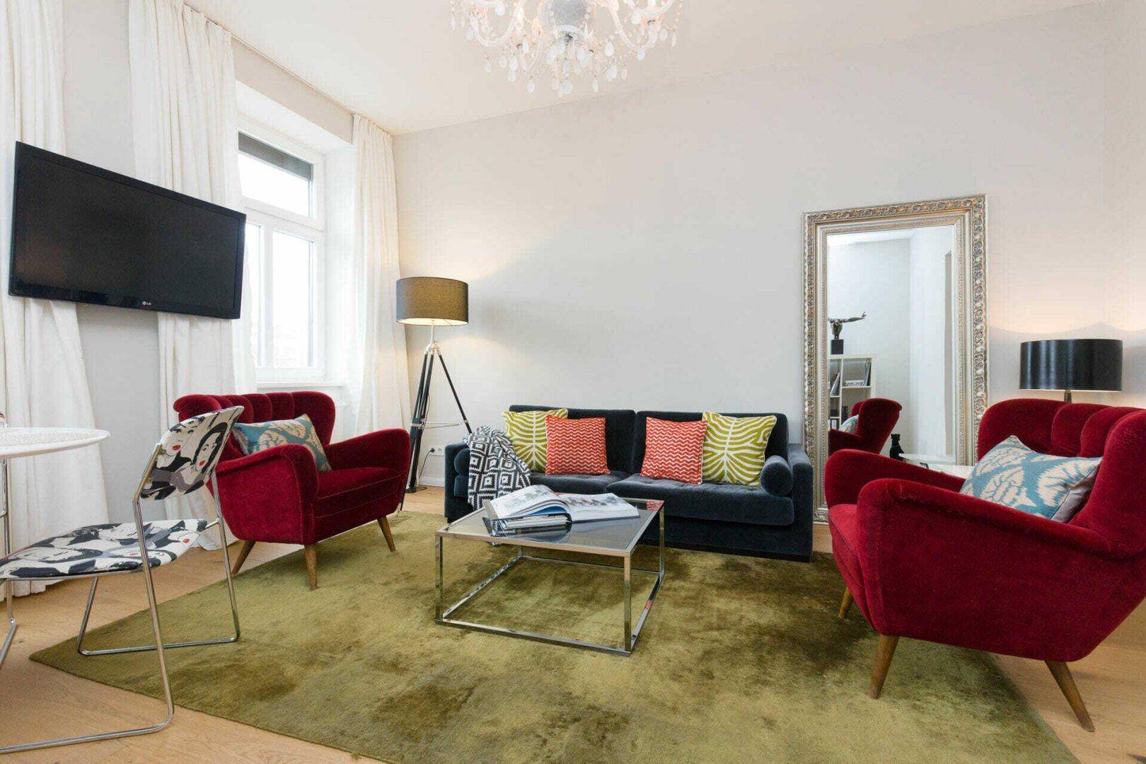 Stilvolles Wohnzimmer mit bequemen Sofas, roten Sesseln und einem großen Spiegel.