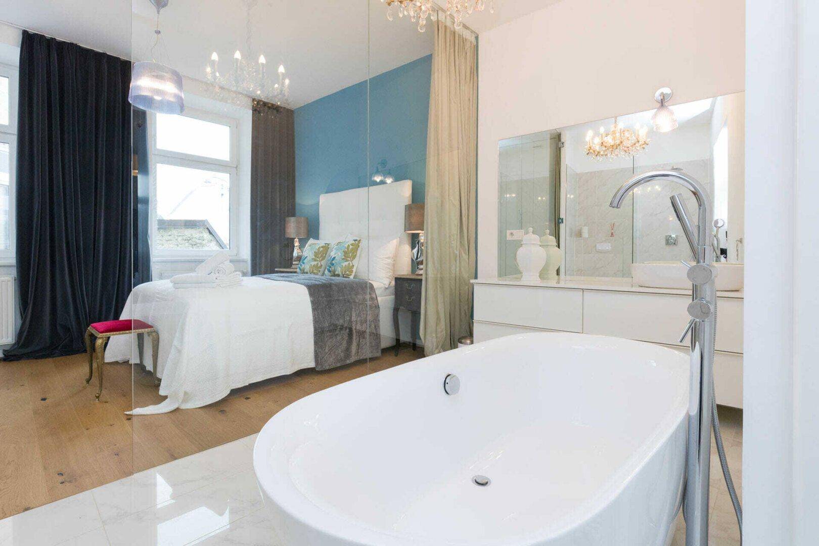 Schlafzimmer mit offener Verbindung zum luxuriösen Badezimmer, blauer Wand und Holzboden.