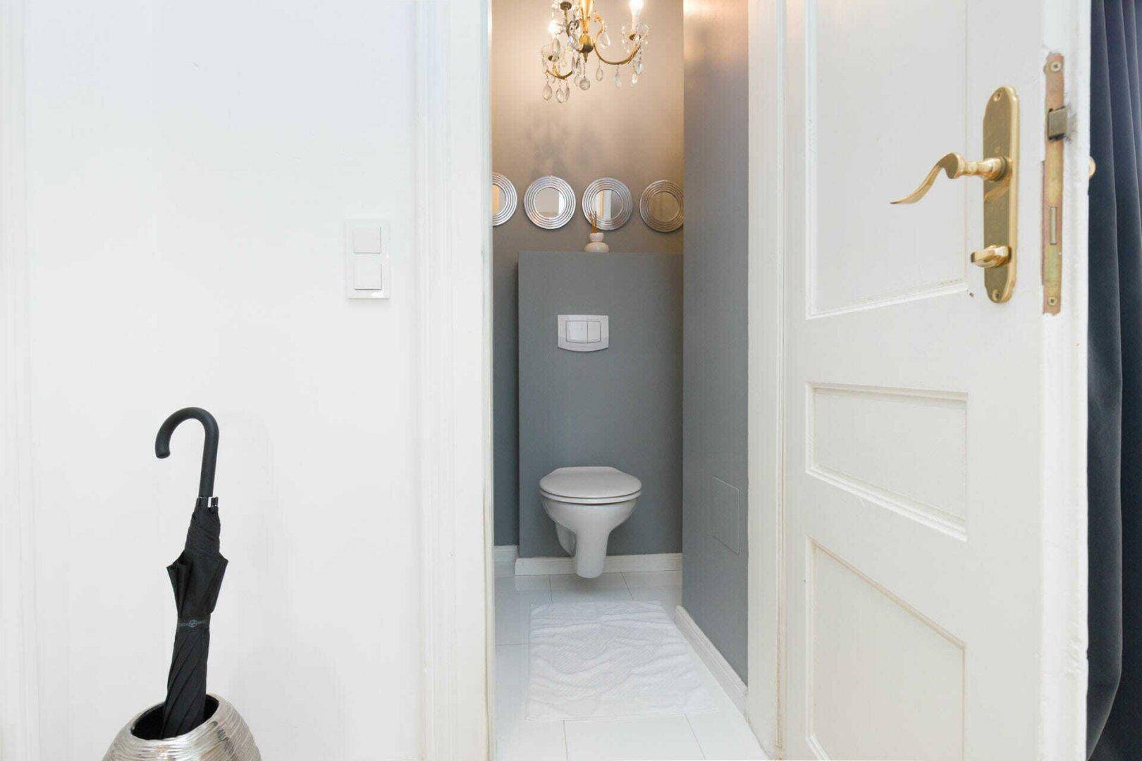 Kleines Gäste-WC mit Wand-WC und grauen Wänden, vom Flur aus zugänglich.