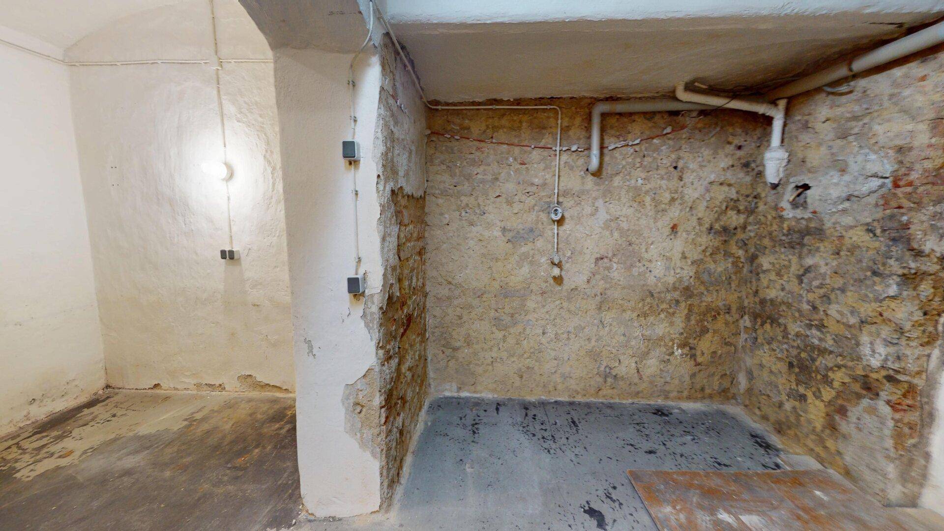 Rustikaler Kellerraum mit unverputzten Steinwänden und sichtbaren Rohren an der Decke.