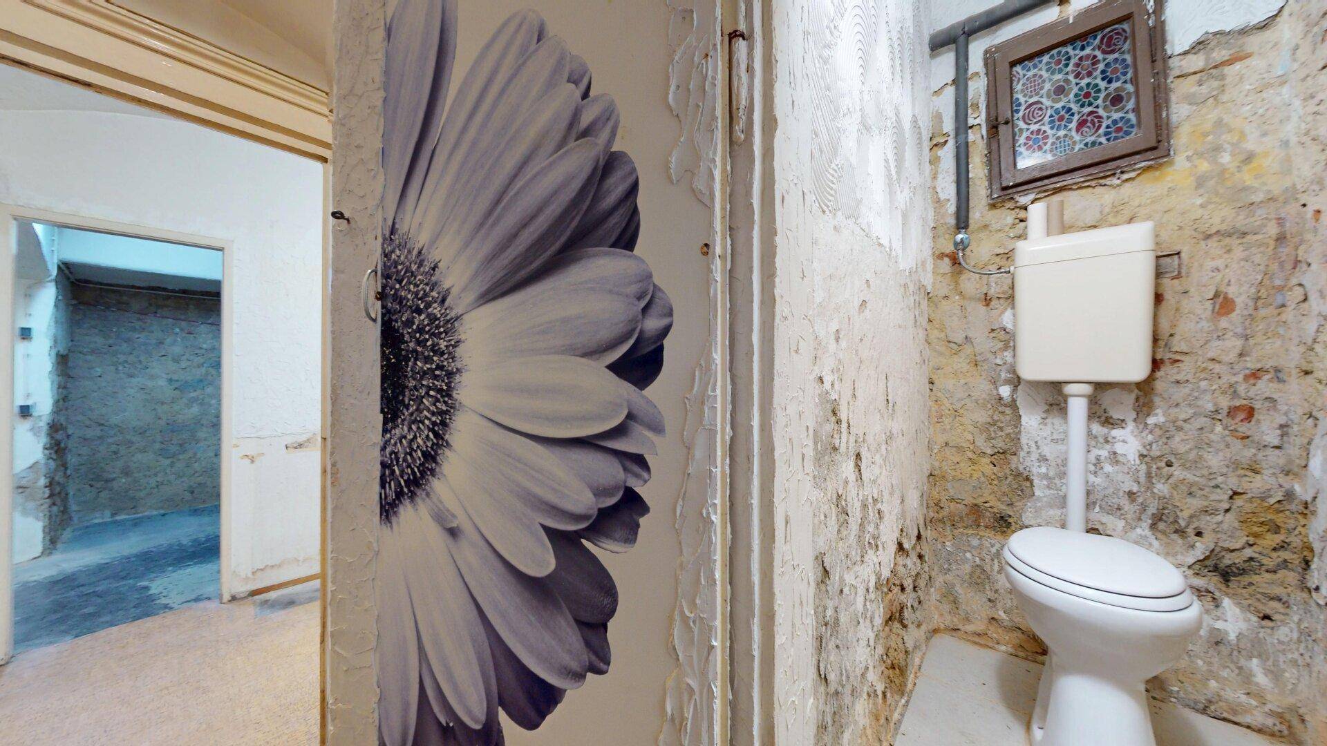 Einfache Toilette im Kellerbereich mit rauen Wänden und einem kleinen Fenster.