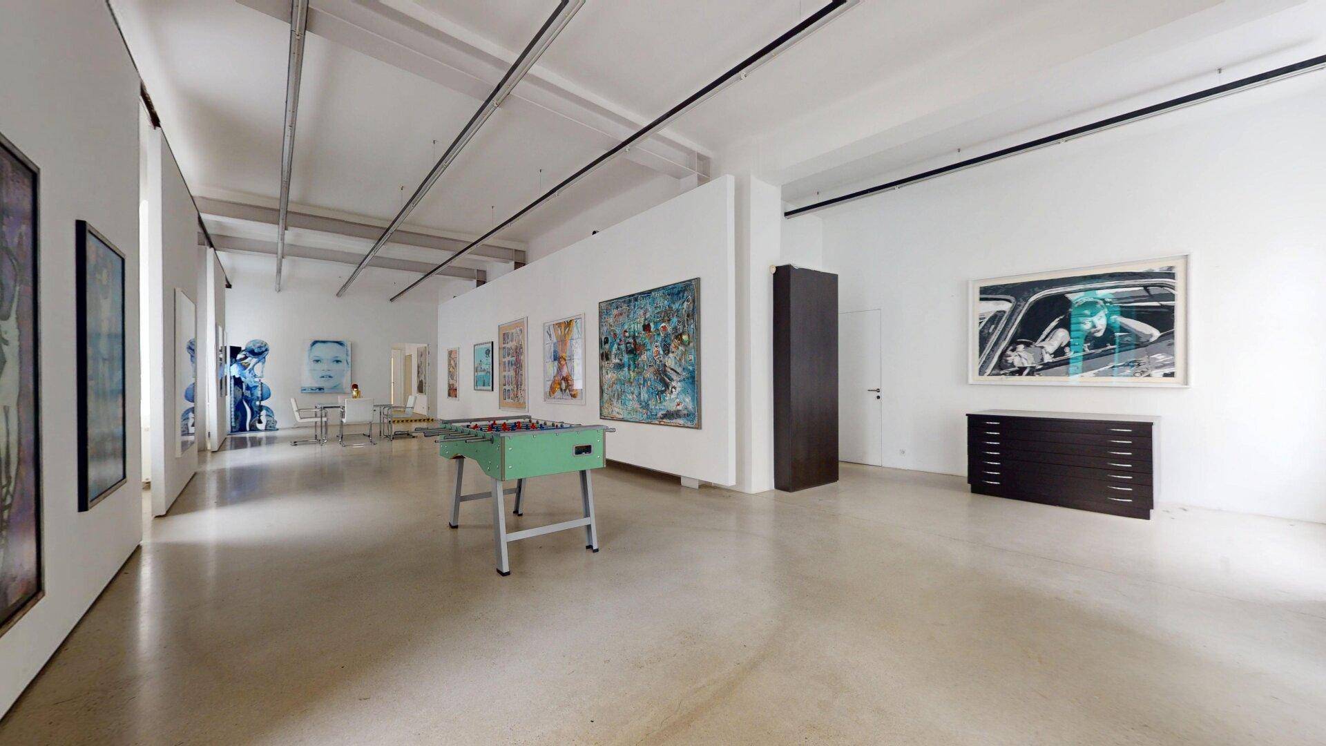 Weitläufiger Ausstellungsraum mit verschiedenen Kunstwerken und einem Tischfußballtisch in der Mitte.