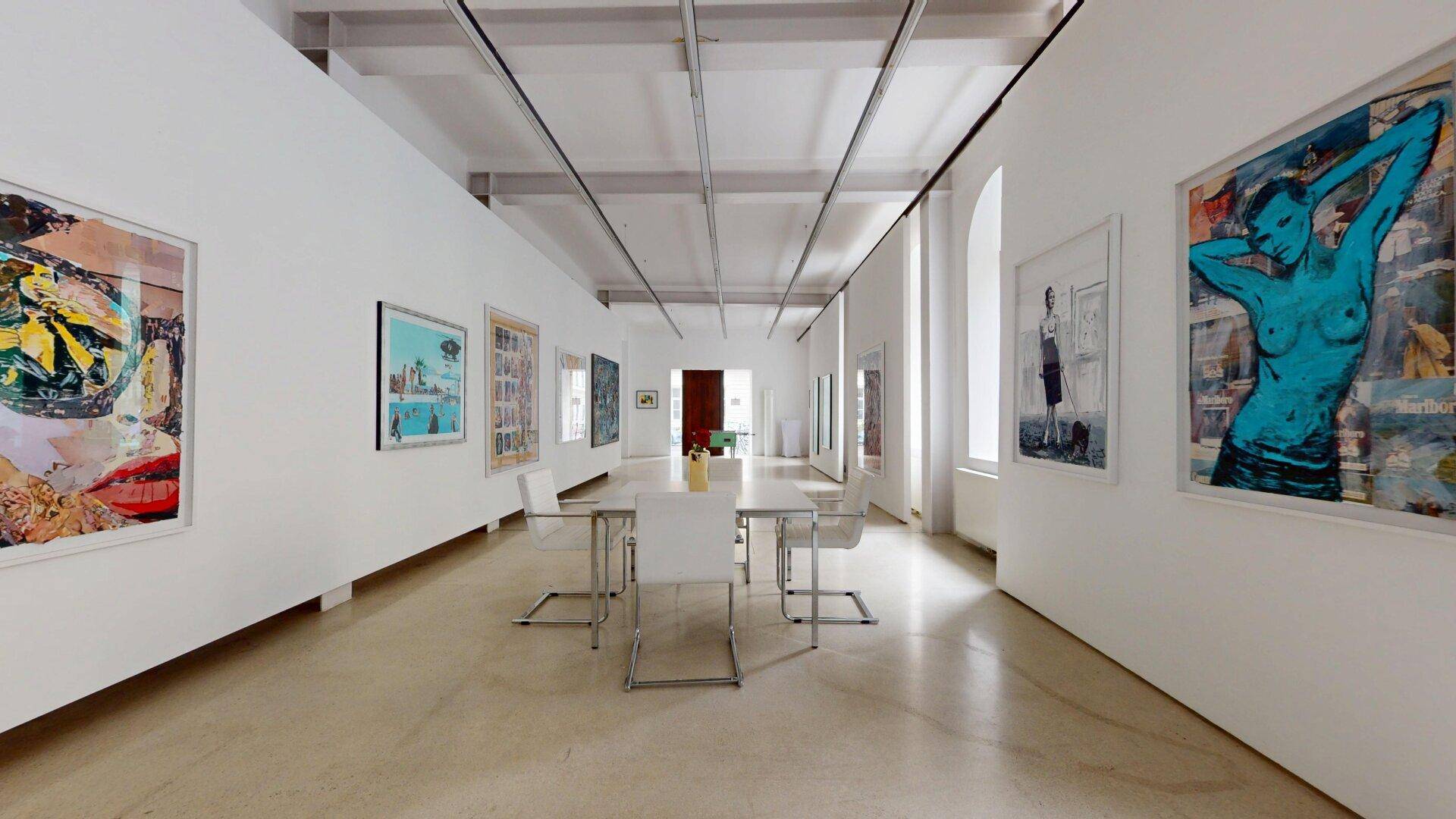 Geräumiger, heller Ausstellungsraum mit Kunstwerken, hohen Fenstern und einem modernen Esstisch.