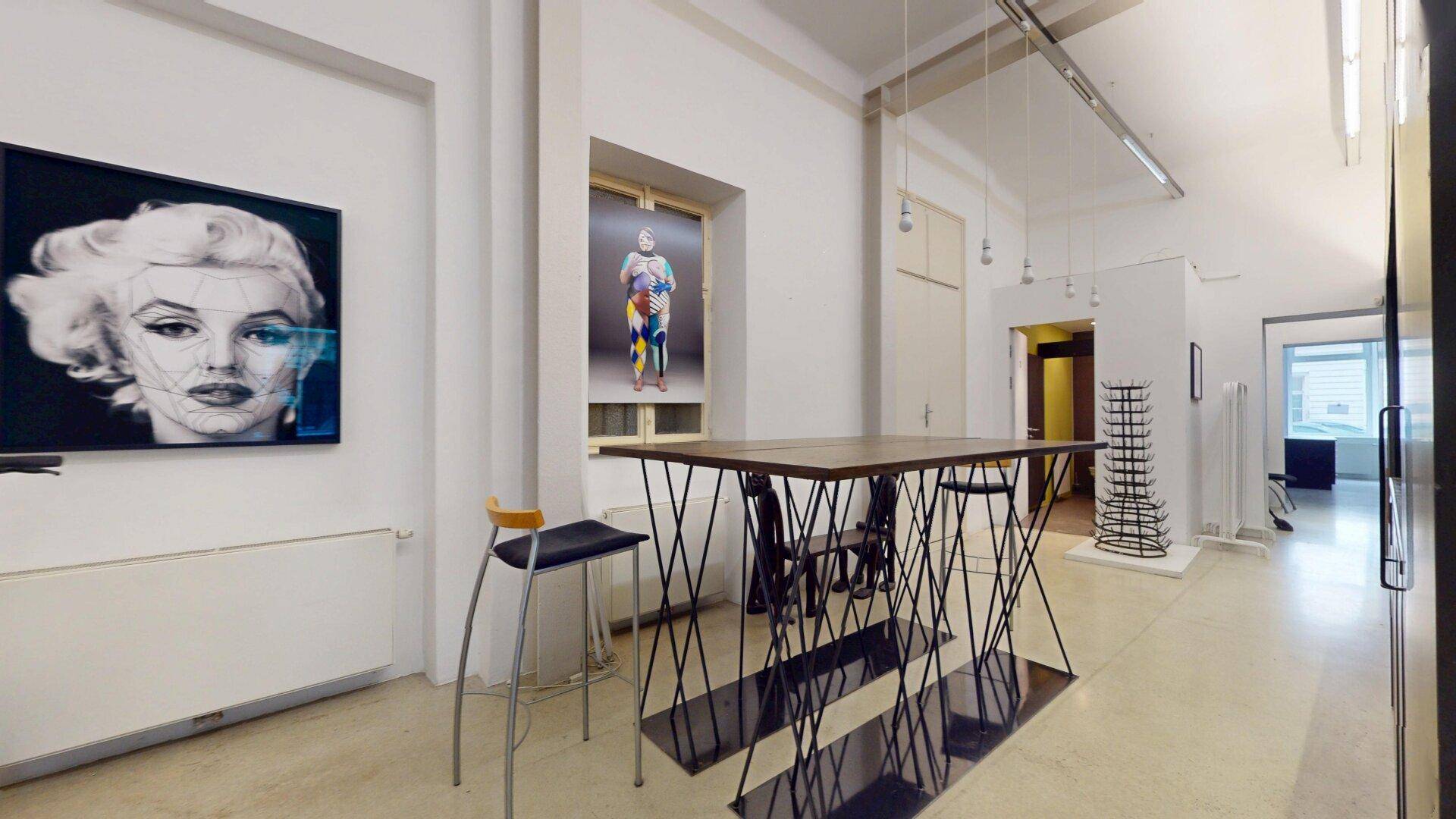 Langer, heller Raum mit Kunstwerken, einem hohen Tisch und Barhockern, ideal für informelle Treffen.