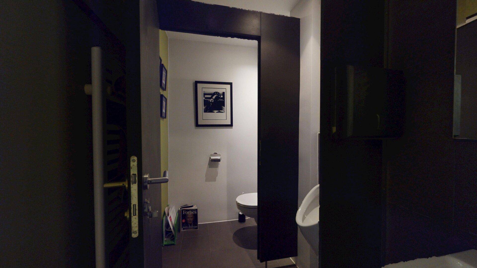 Modernes Gäste-WC mit Toilette und Urinal, ausgestattet mit dunklen Fliesen.