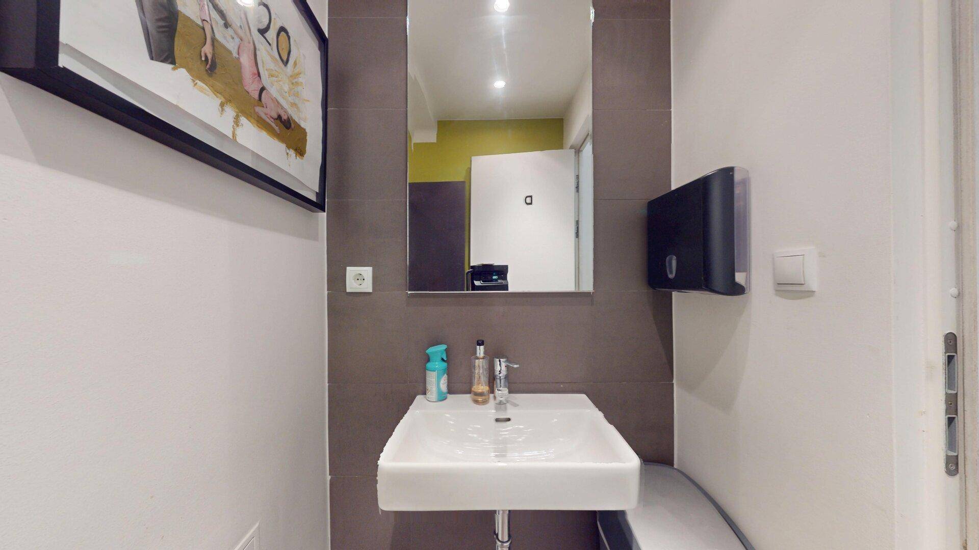 Modern gefliestes Gäste-WC mit kleinem Waschbecken, Spiegel und Seifenspender.
