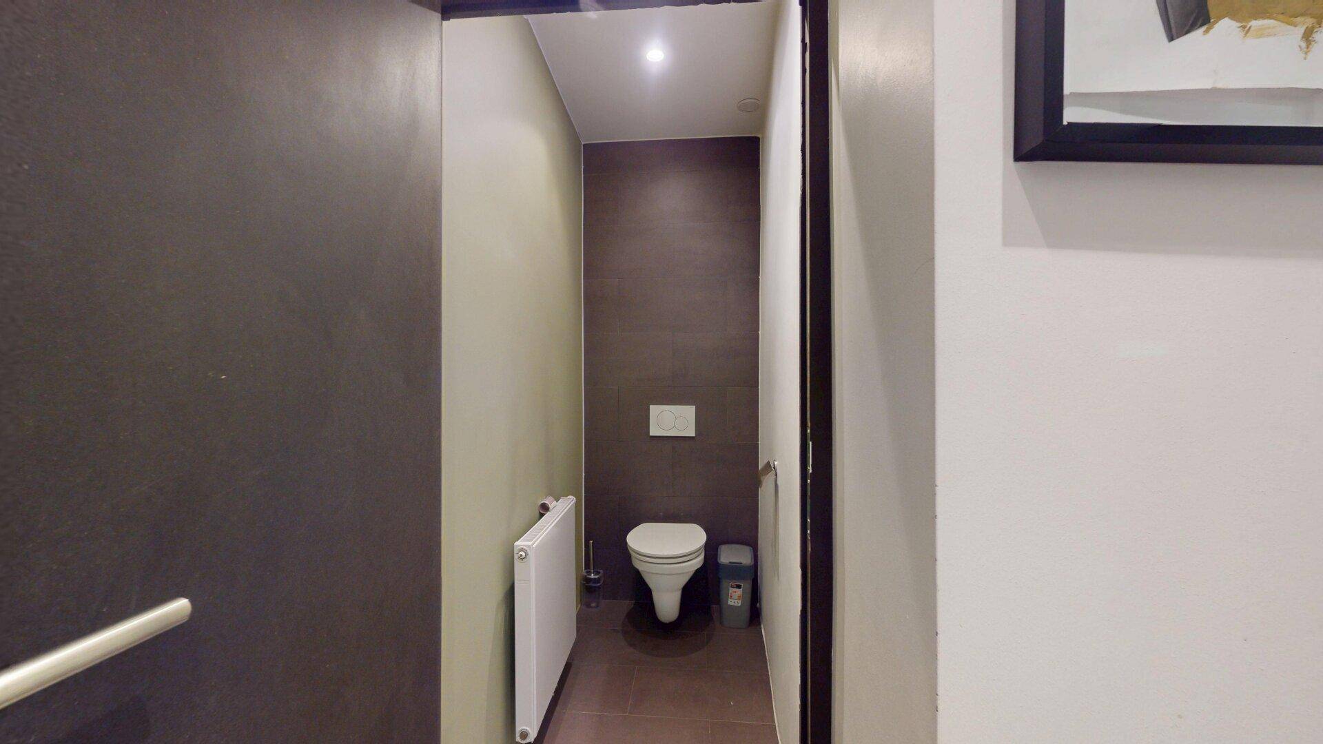 Modernes Gäste-WC mit wandhängender Toilette, Heizkörper und dunklen Fliesen.