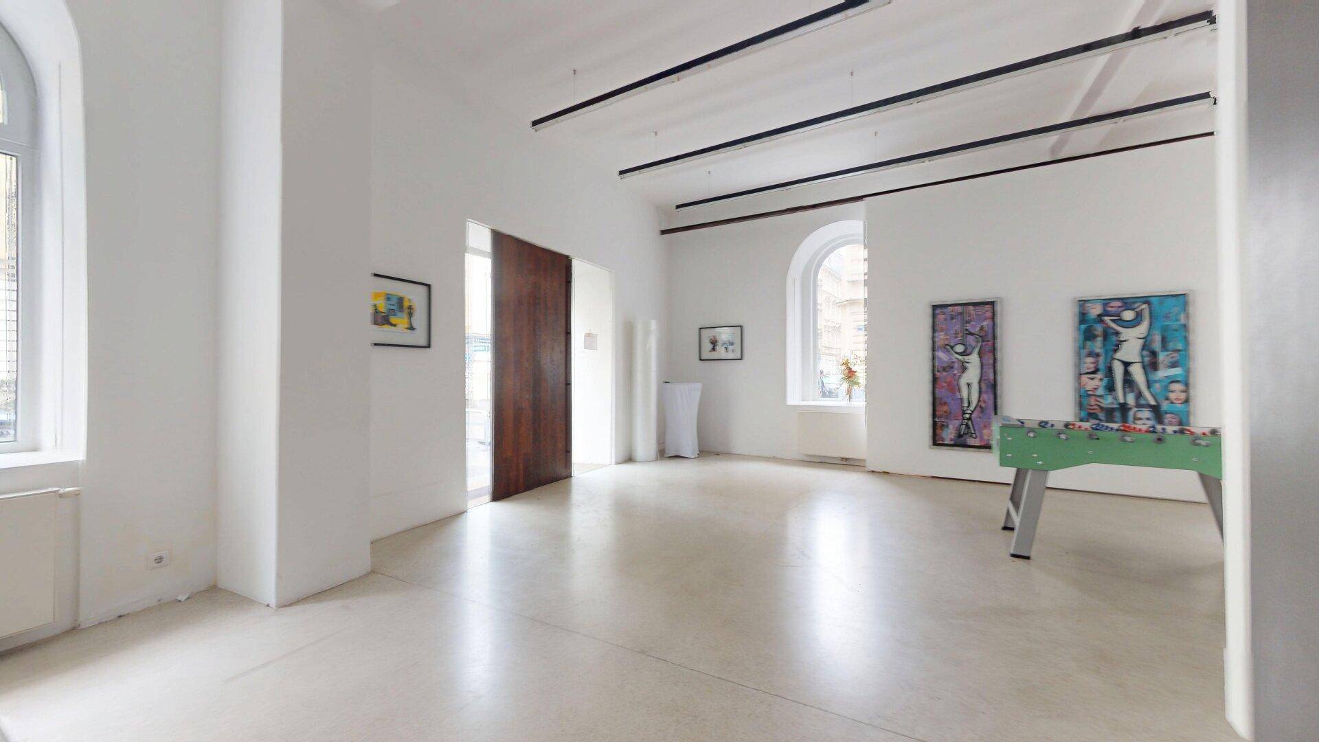 Geräumiger, heller Raum mit hohen Fenstern, Kunstwerken und einem Tischfußballspiel in der Mitte.