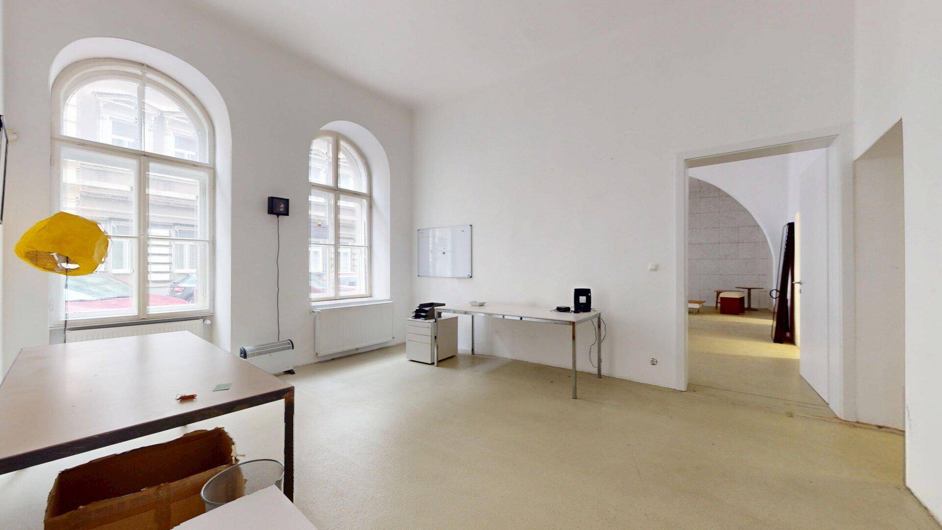Helles Büro mit zwei großen Rundbogenfenstern, Schreibtischen und einem Durchgang zu weiteren Räumen.