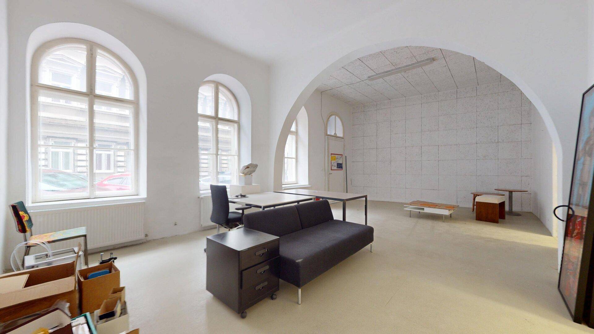Großer, heller Büroraum mit hohen Rundbogenfenstern, einem Sofa und einem gewölbten Deckenbereich.