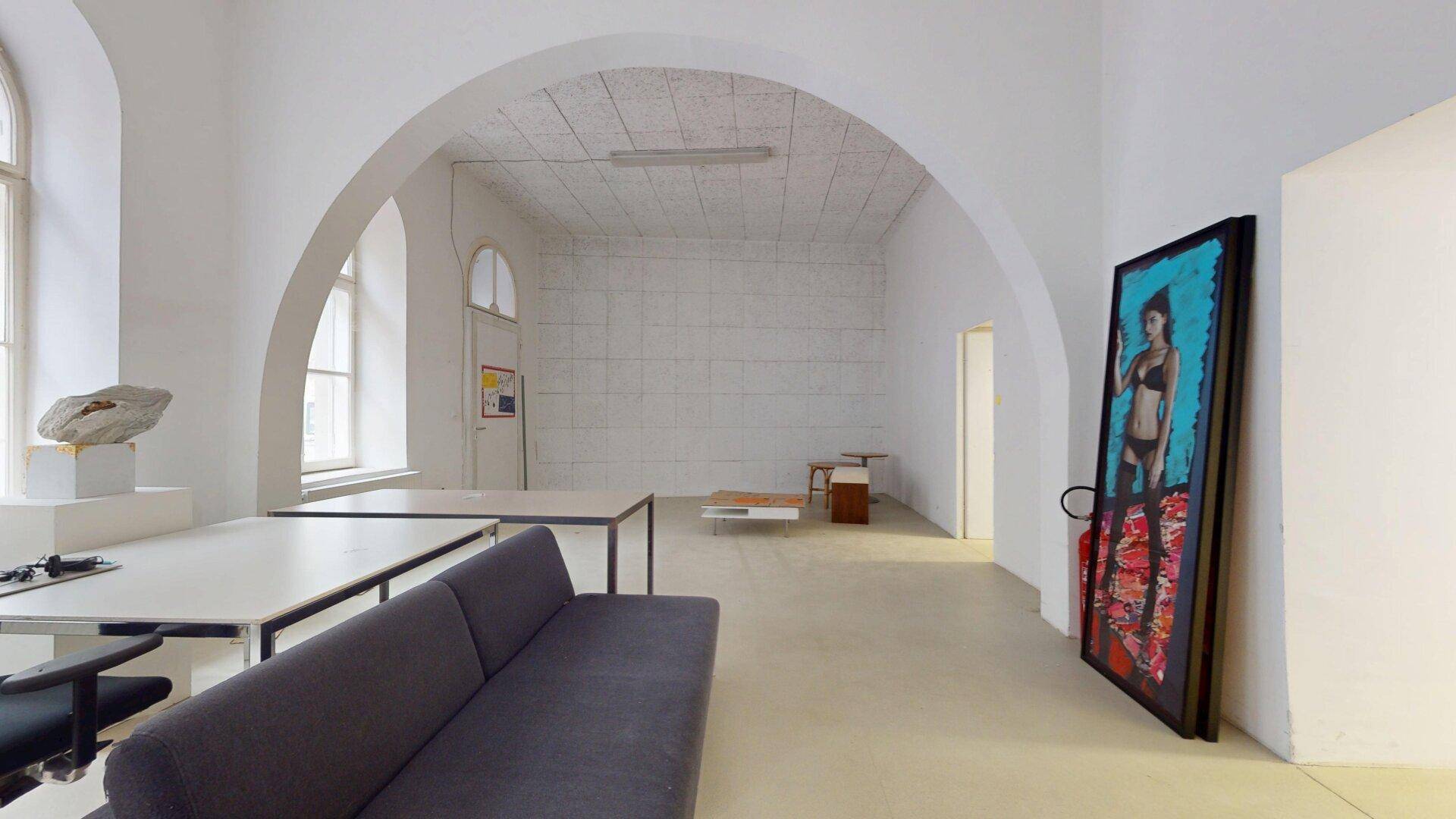 Geräumiges Büro mit gewölbter Decke, hohen Fenstern und einem Sofa, ideal für kreative Arbeit.