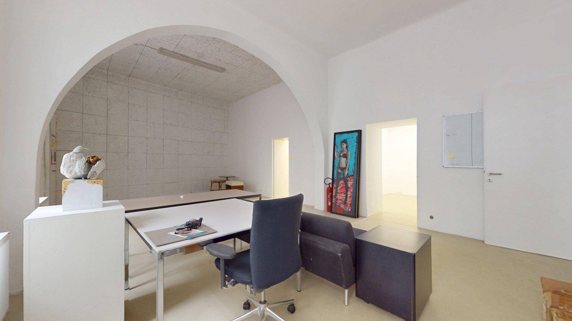 Helles Büro mit gewölbter Decke, Schreibtisch, Bürostuhl und einem Kunstwerk an der Wand.