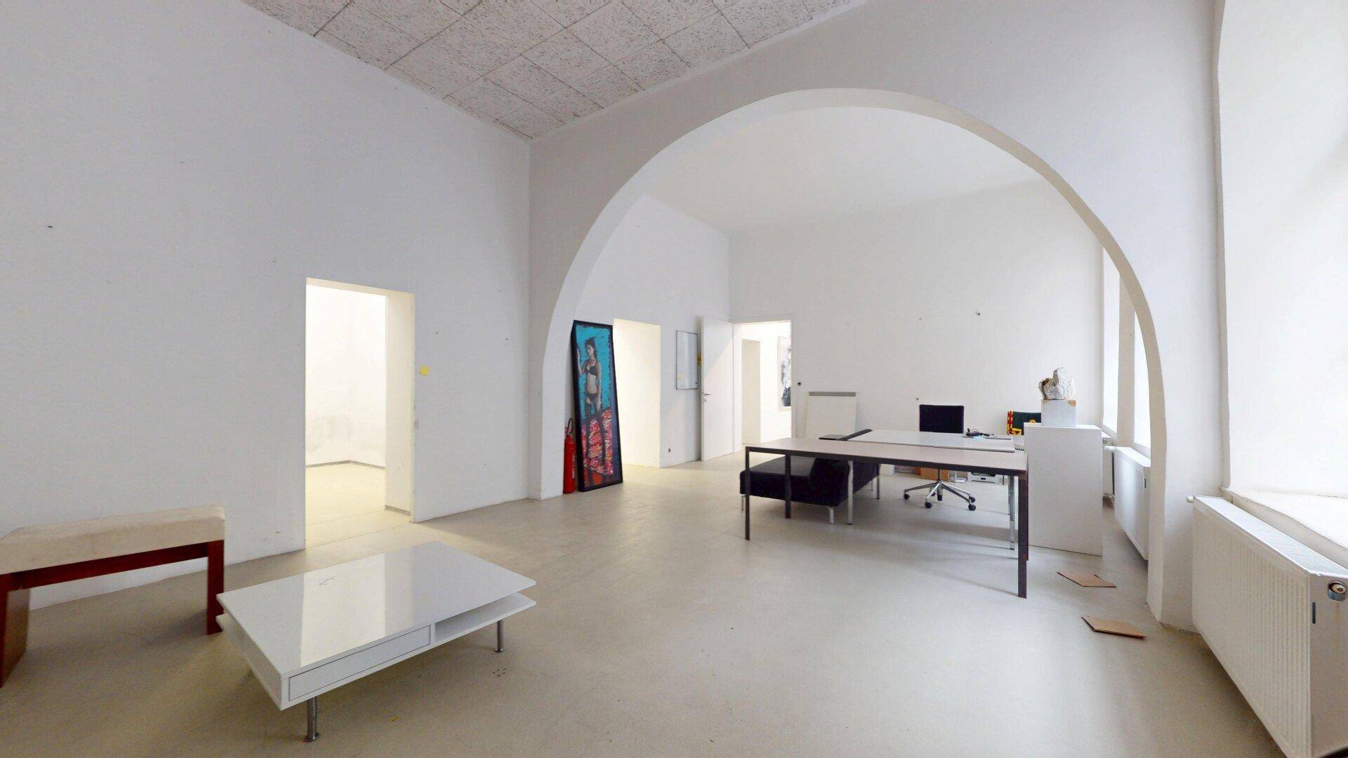 Großer, heller Büroraum mit gewölbter Decke, Schreibtischen und einem modernen Couchtisch.