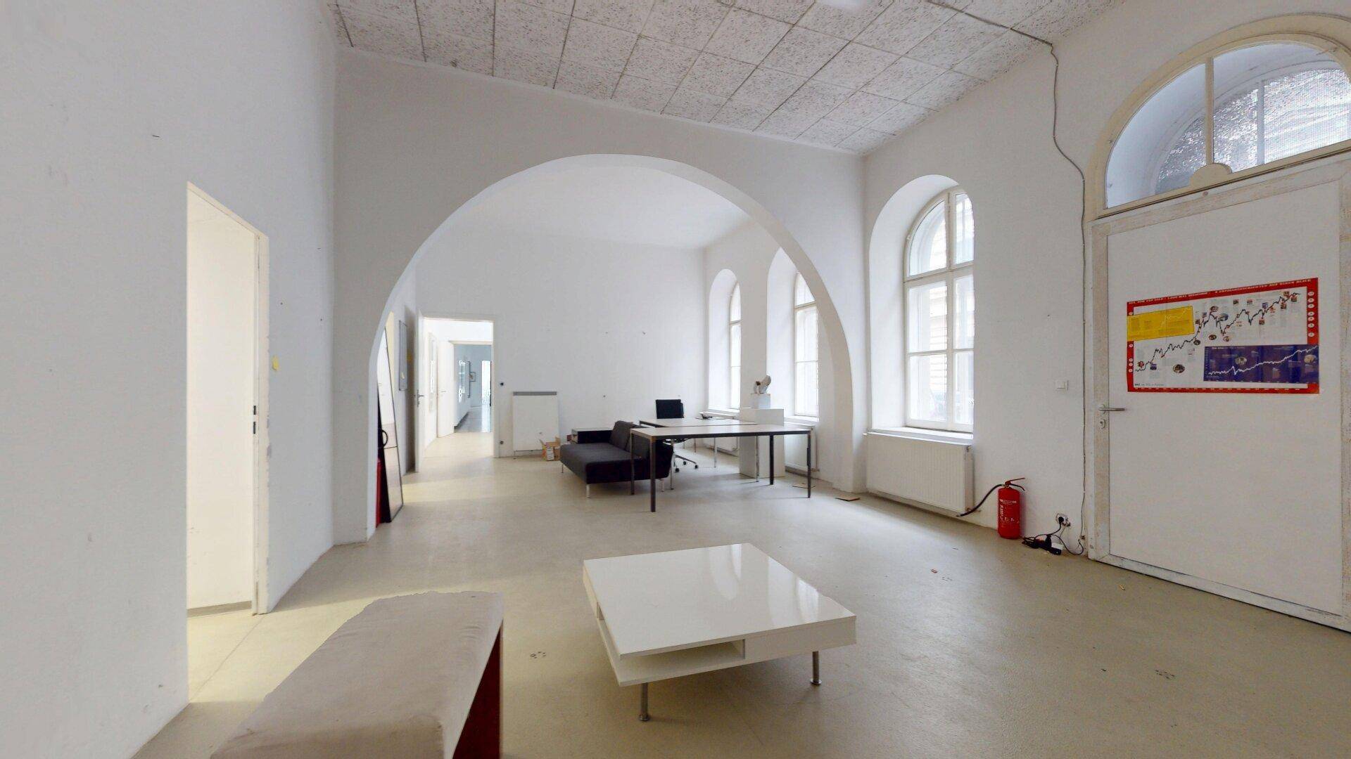 Geräumiger, heller Büroraum mit hohen Decken, Rundbogenfenstern und minimalistischer Einrichtung.
