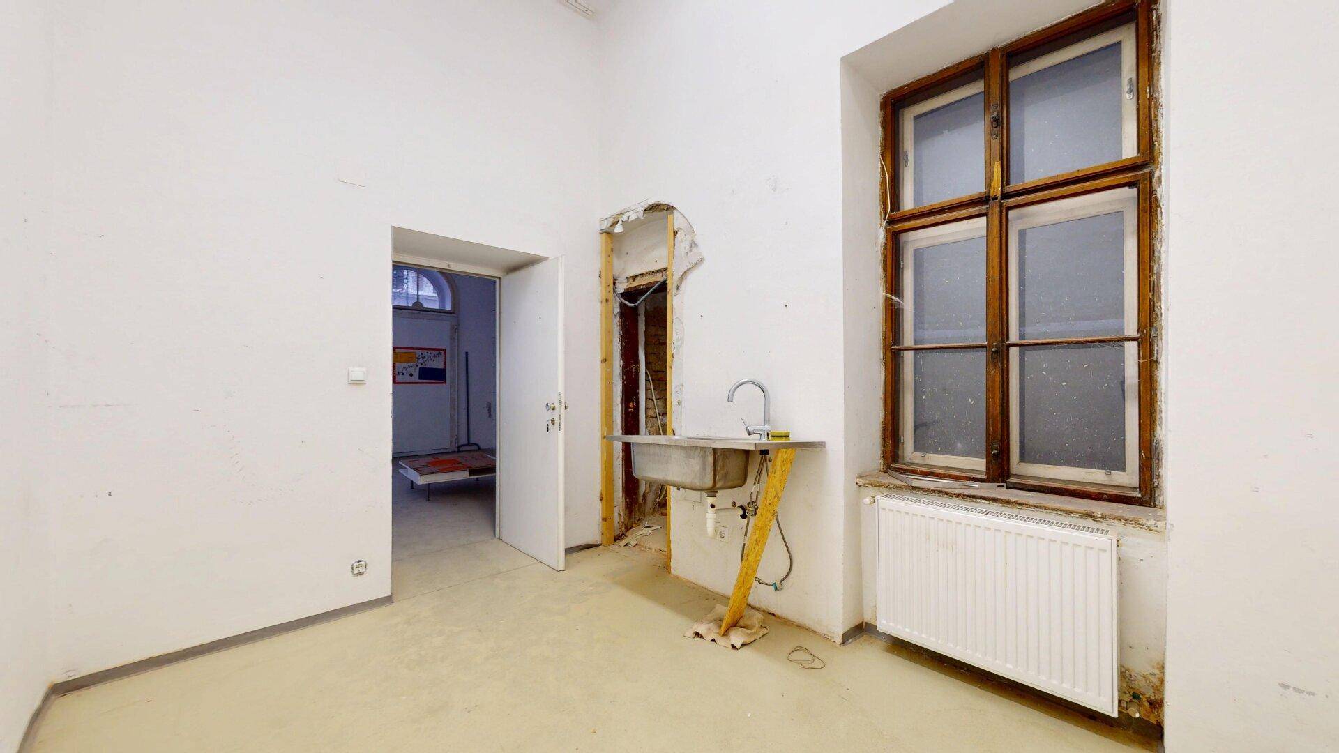 Unfertiger Raum mit einem Waschbecken, einem alten Fenster und einem Heizkörper.