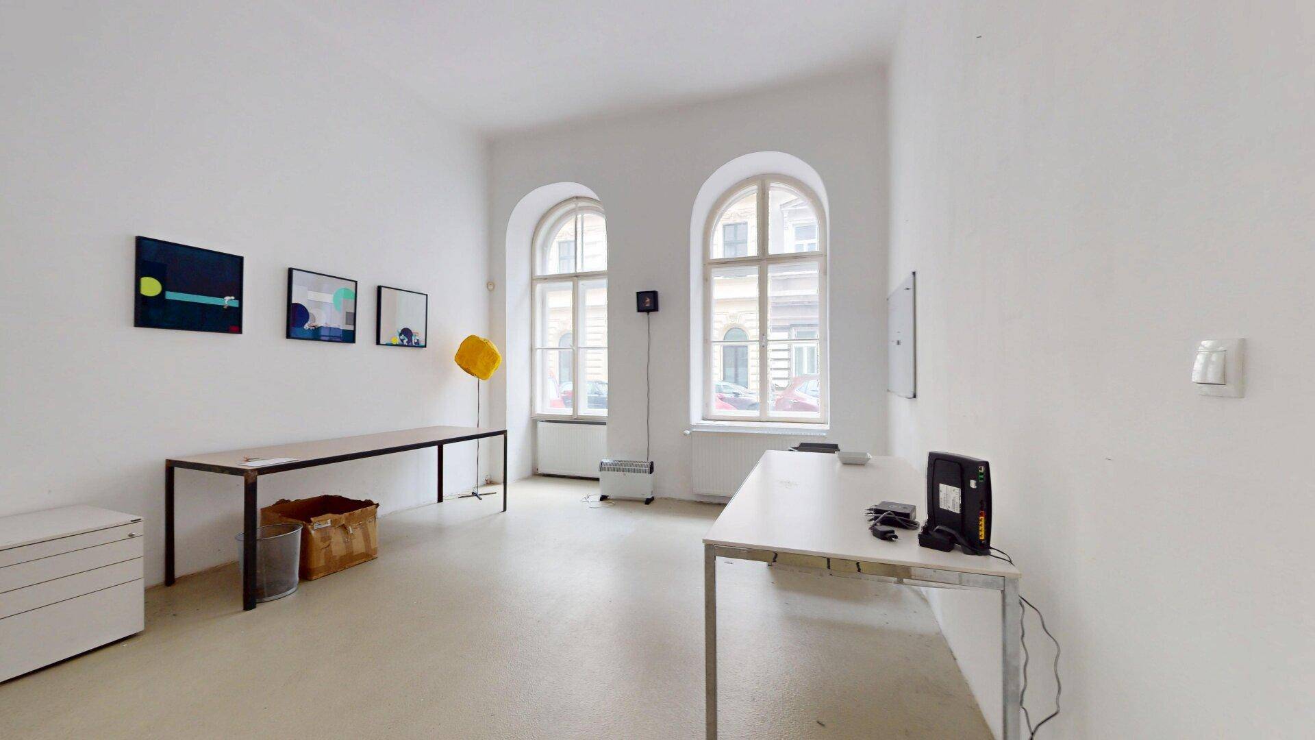 Heller Bürobereich mit zwei großen Fenstern, Schreibtischen und moderner Kunst an den Wänden.