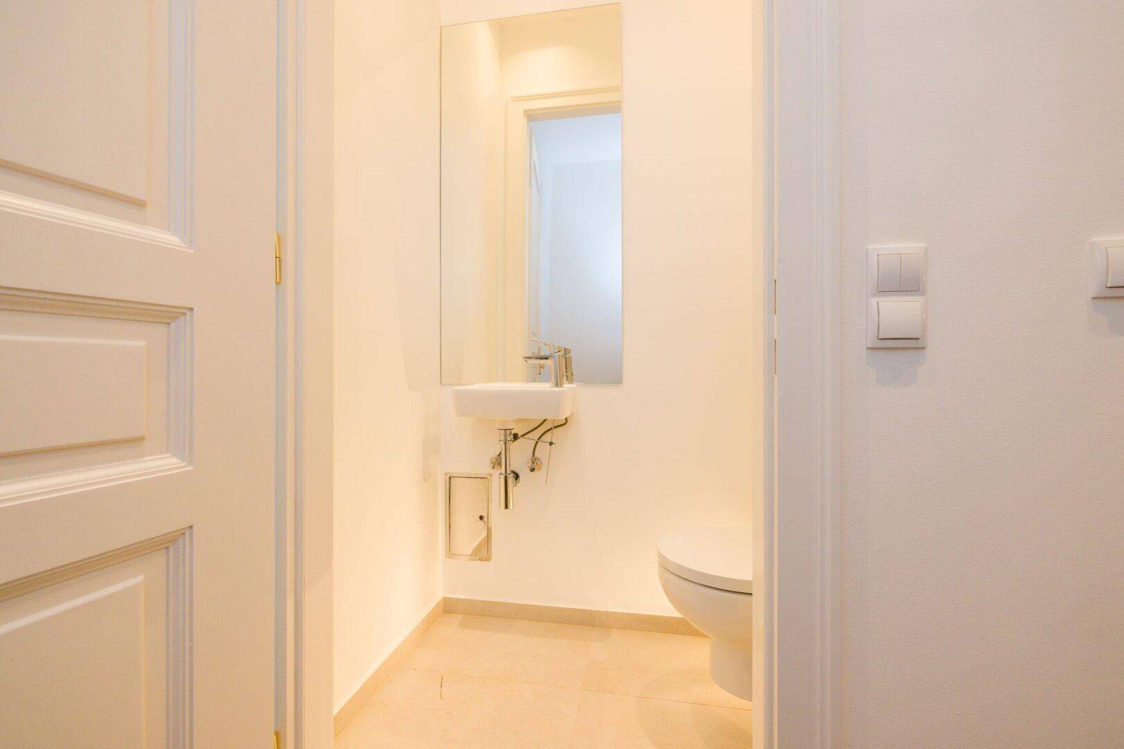 Separates Gäste-WC mit wandhängender Toilette und kleinem Handwaschbecken.
