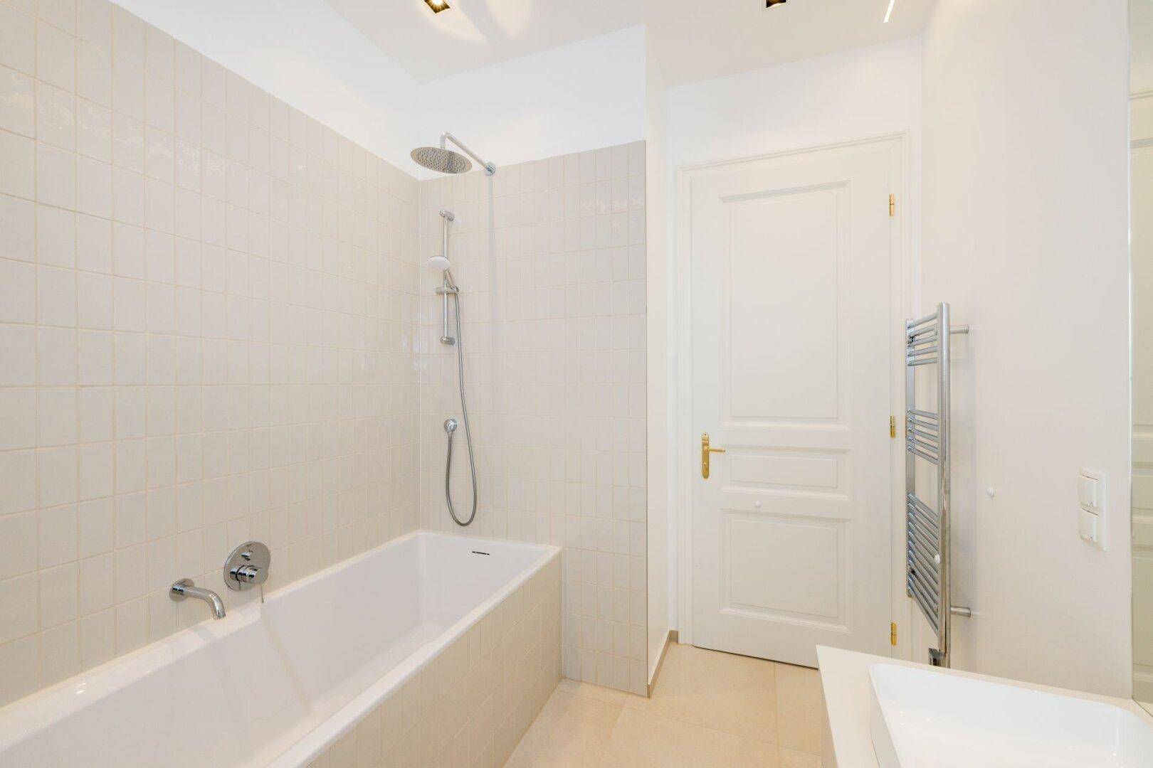 Modernes Badezimmer mit Badewanne, Duschfunktion und beheiztem Handtuchhalter.