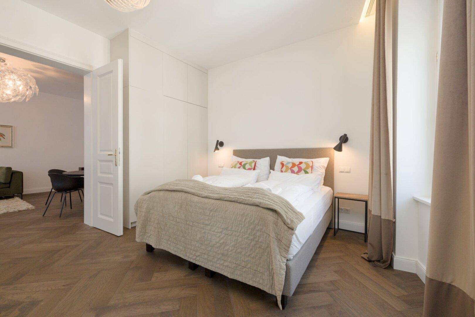 Helles Schlafzimmer mit Doppelbett, Einbauschränken und Zugang zum Wohnbereich.