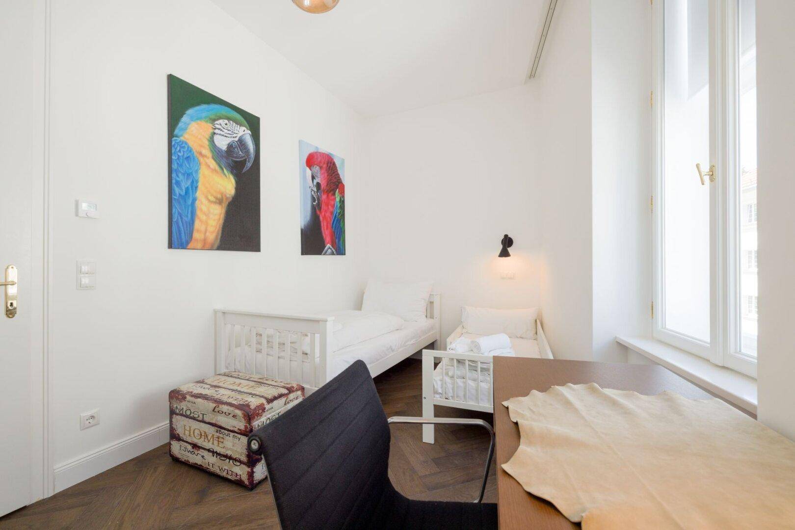 Schlafzimmer mit zwei Einzelbetten, Schreibtisch und farbenfrohen Kunstwerken.