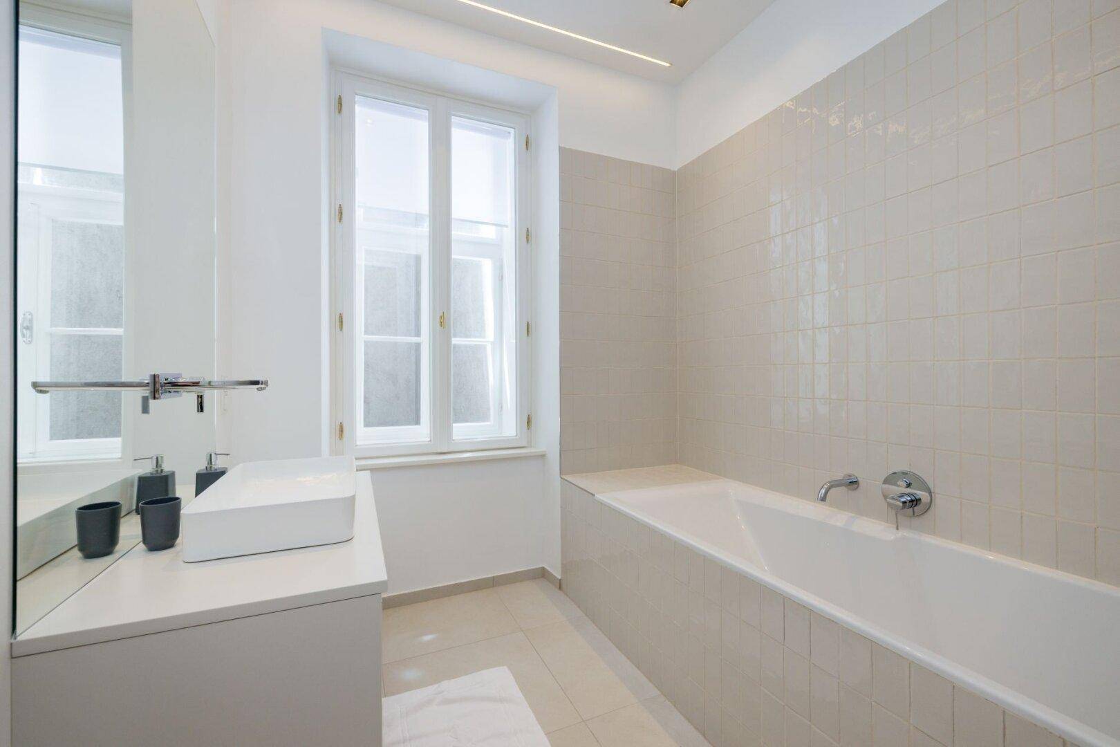 Helles Badezimmer mit Fenster, modernem Waschbecken und Badewanne.