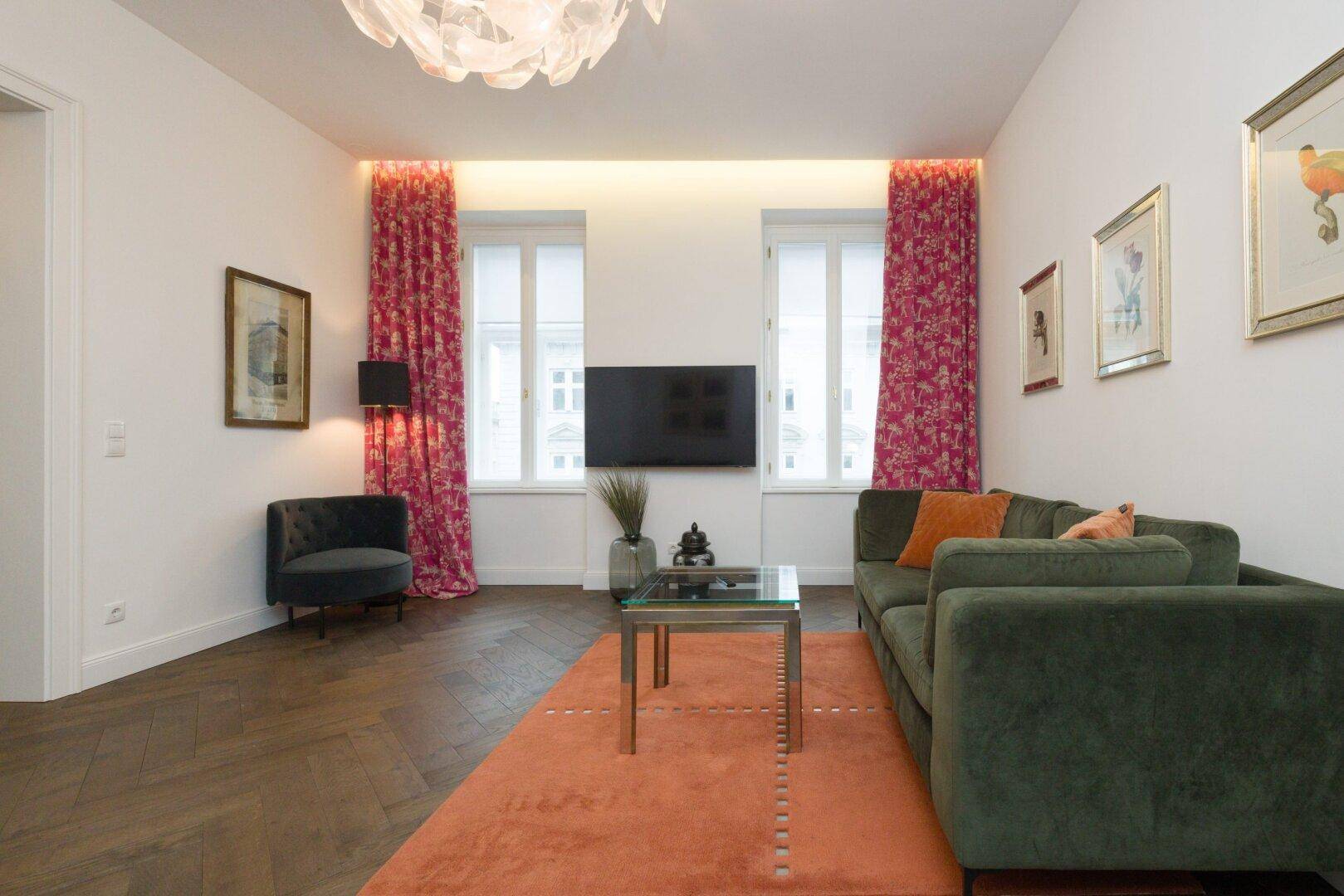 Heller Wohnbereich mit bequemer Couch, Fernseher und dekorativen Vorhängen.