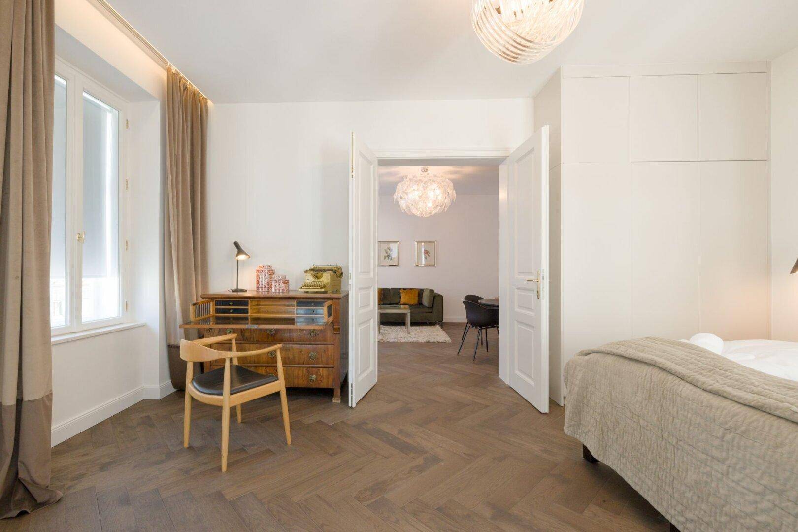 Schlafzimmer mit Arbeitsbereich, Doppelbett und Blick in den Wohnbereich.