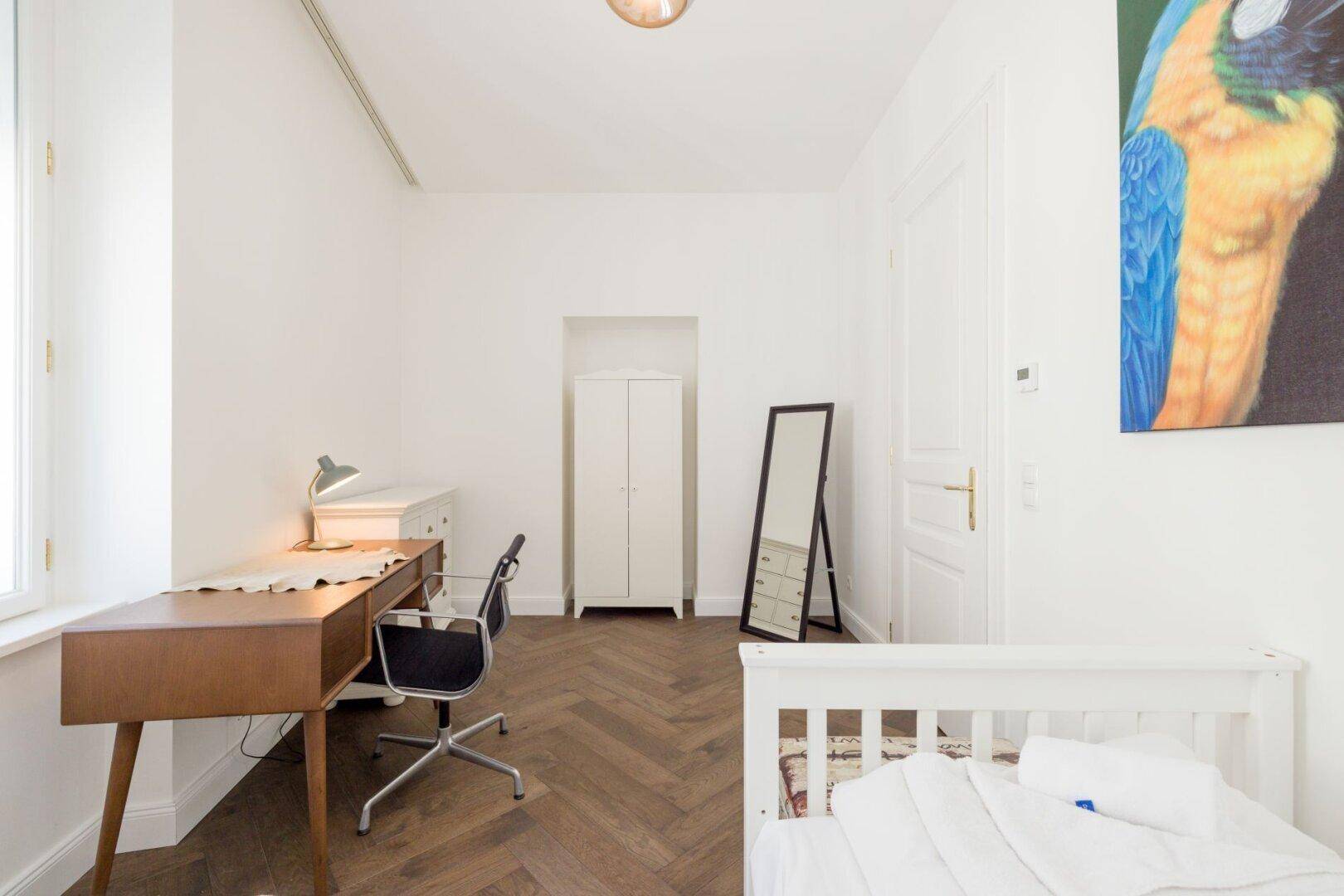 Helles Schlafzimmer mit Einzelbett, Schreibtisch und großem Wandspiegel.